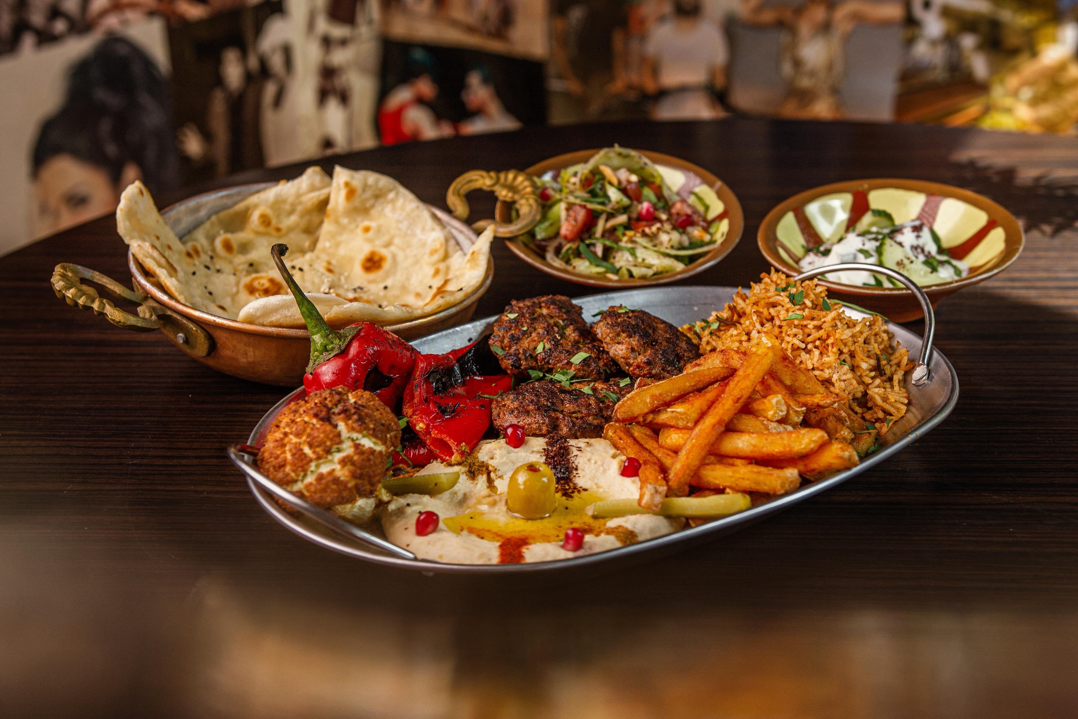 Une assiette de köfte avec du houmous, des quartiers de pommes de terre, du riz, de la salade, du pain arabe et de la sauce au yaourt.