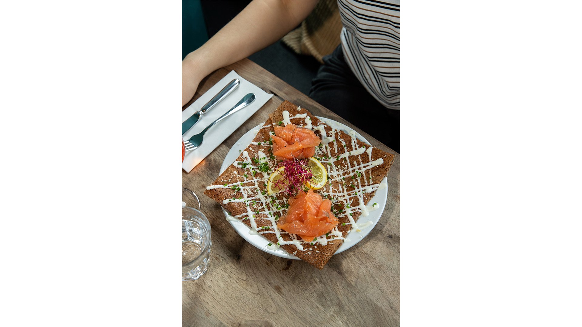 Une galette garnie de saumon fumée posée sur une assiette.