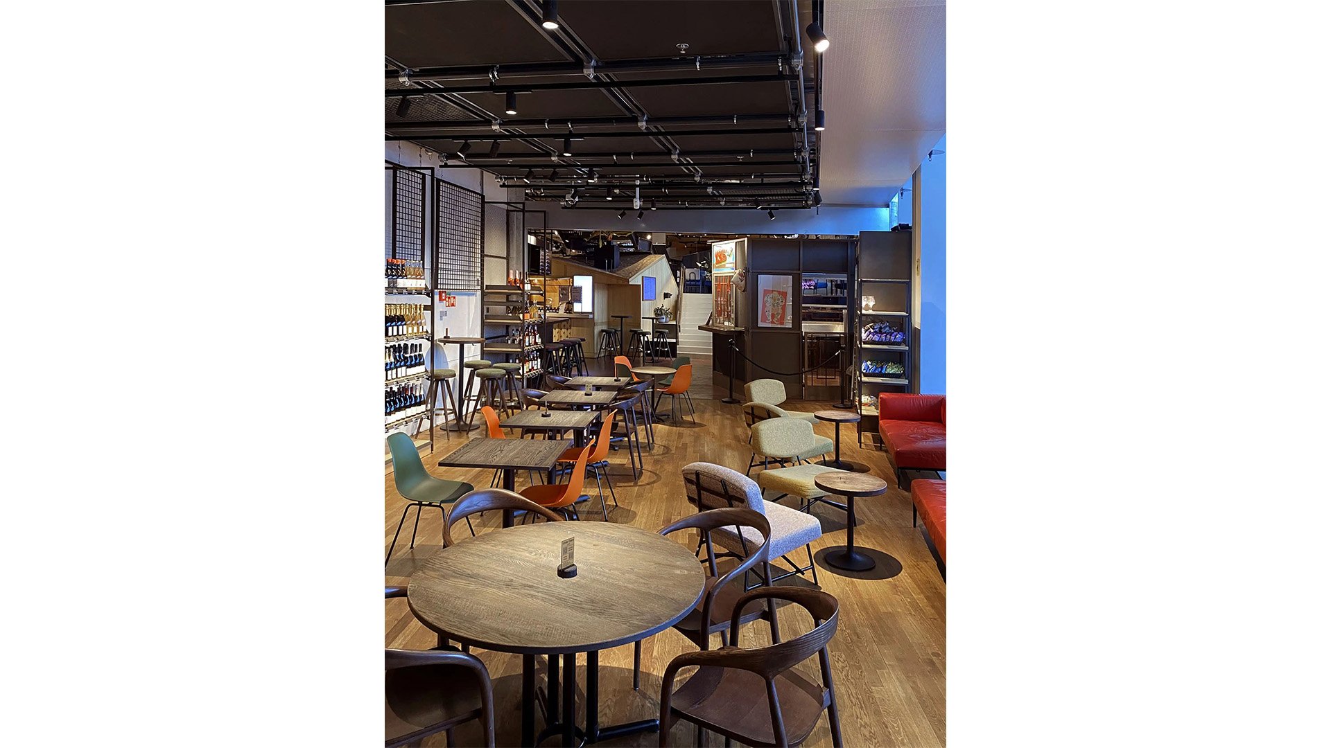 The Bar Beer & Wine Shop avec des tables et des chaises, et des étagères murales remplies de bouteilles de vin.