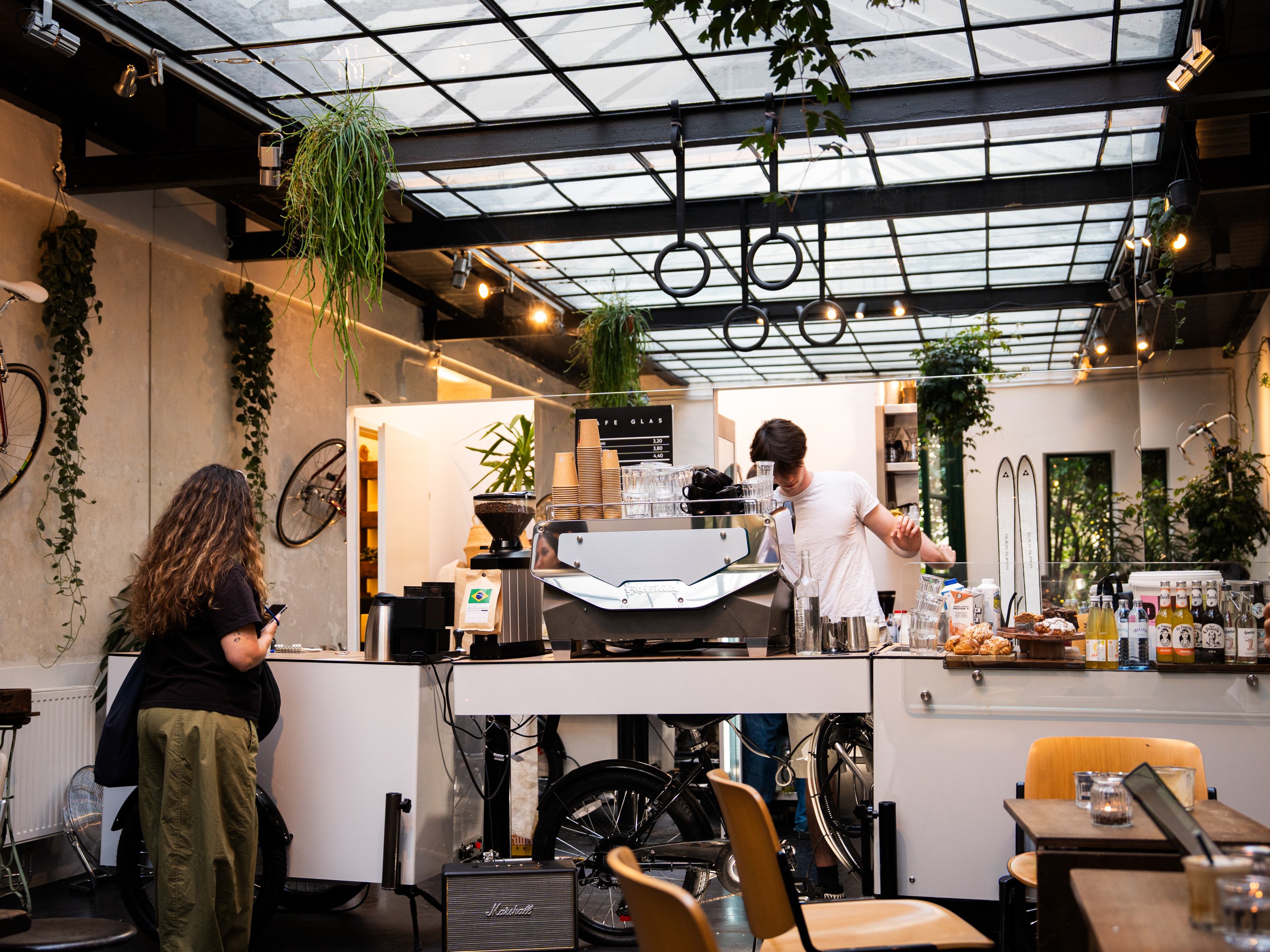 Vue intérieure du Cafe Glas à Vienne, avec machine à expresso, plantes et décoration moderne. Une femme attend de se faire servir son café.