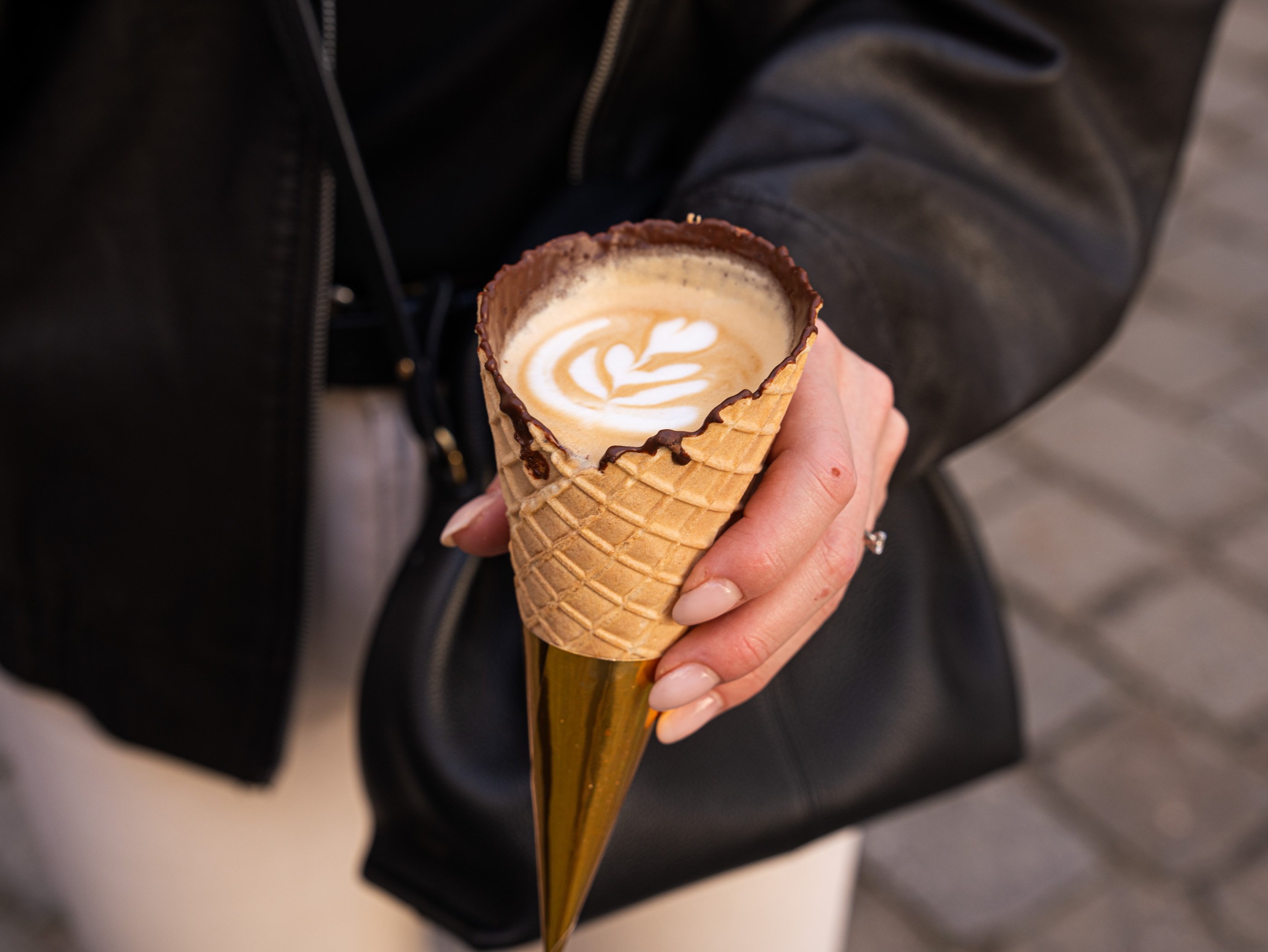Un cappuccino avec latte art servi dans un cornet en gaufrette recouvert de chocolat à l’intérieur.