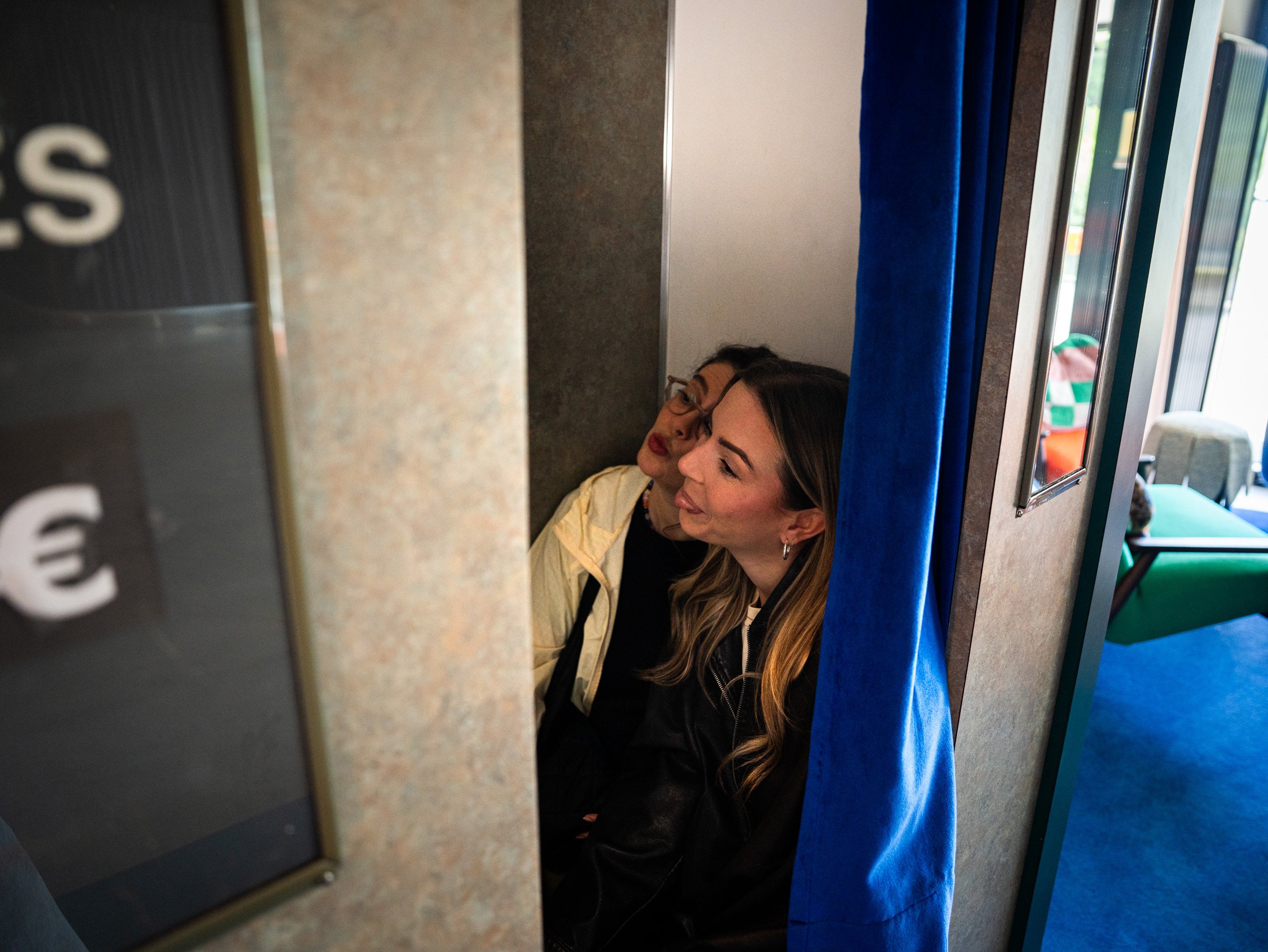 Deux femmes se font prendre en photo dans un photomaton sombre avec rideau bleu, dans le 25hours Hotel, à Vienne.