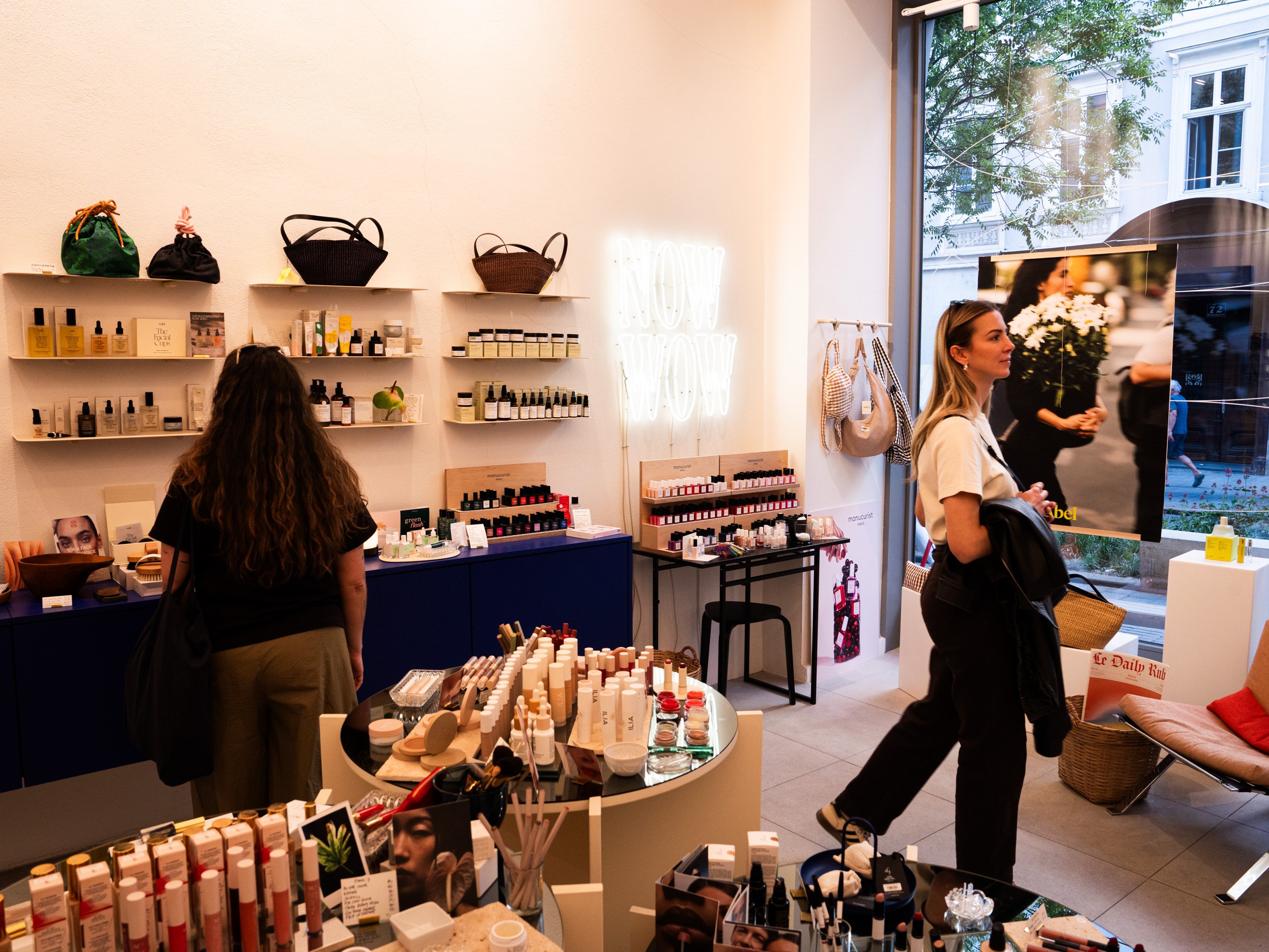 À Vienne, deux femmes explorent un magasin de cosmétique lumineux avec produits de soins, parfums et étagères décoratives.
