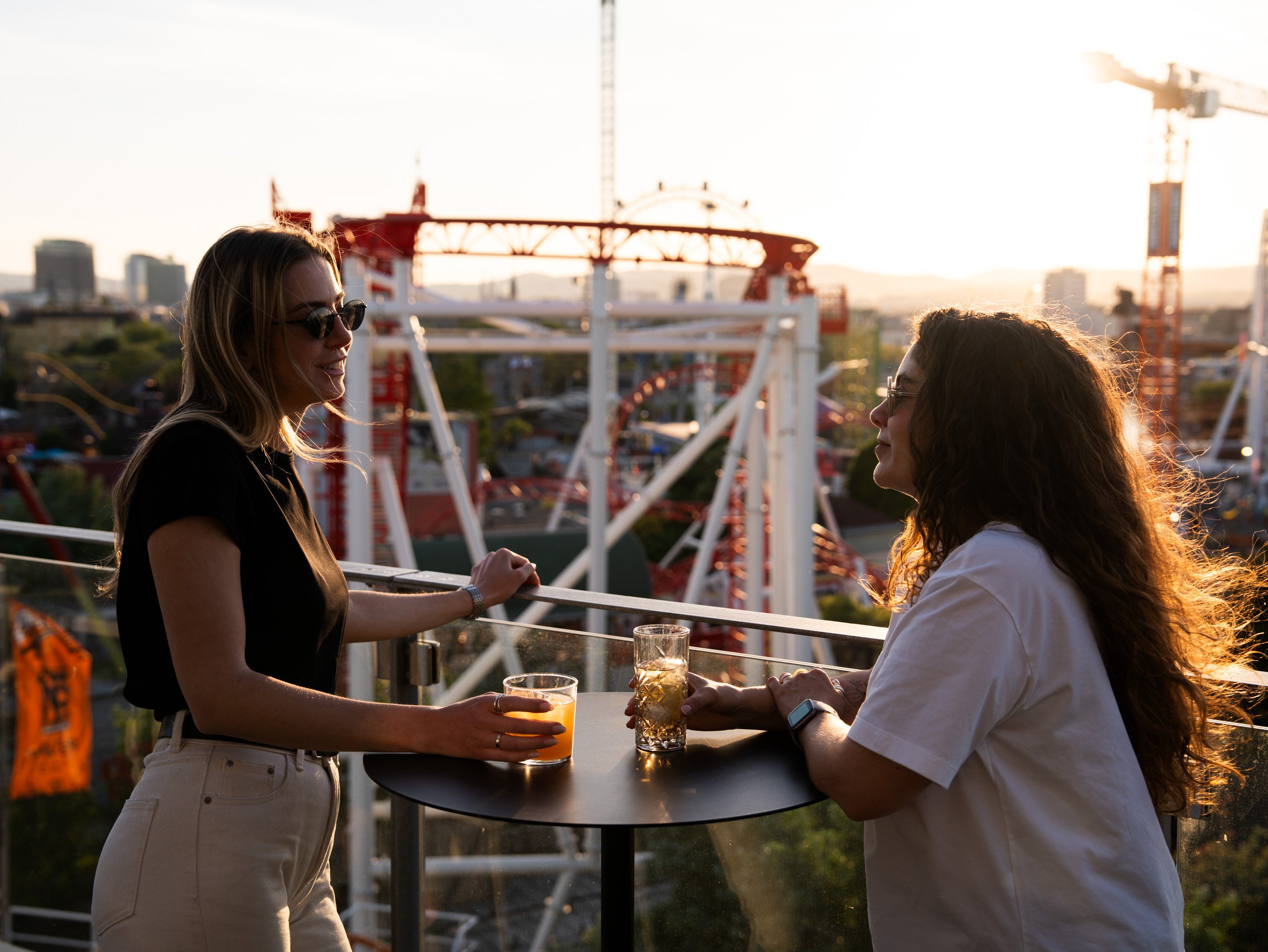 Deux femmes en train de boire un verre sur le toit-terrasse de l’hôtel Zoku, à Vienne, avec vue sur le Prater au coucher du soleil.