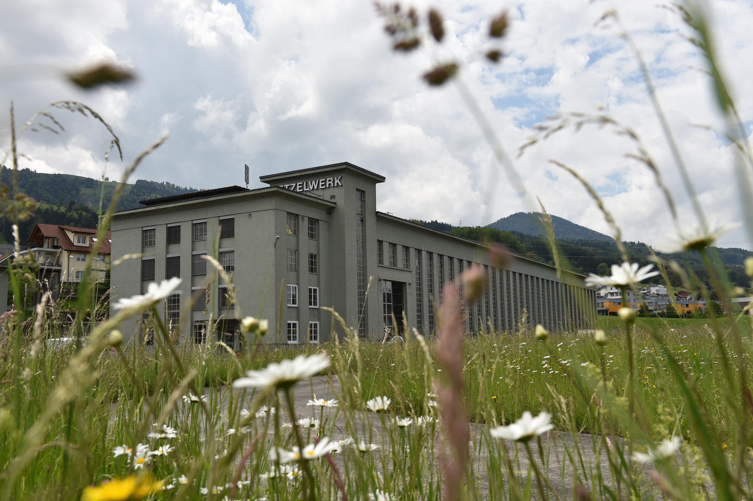 Un grande edificio grigio con lunghe finestre. L’edificio sembra vecchio e presenta la scritta «Etzelwerk», ovvero centrale dell’Etzel. In primo piano ci sono un prato e delle linee elettriche. 