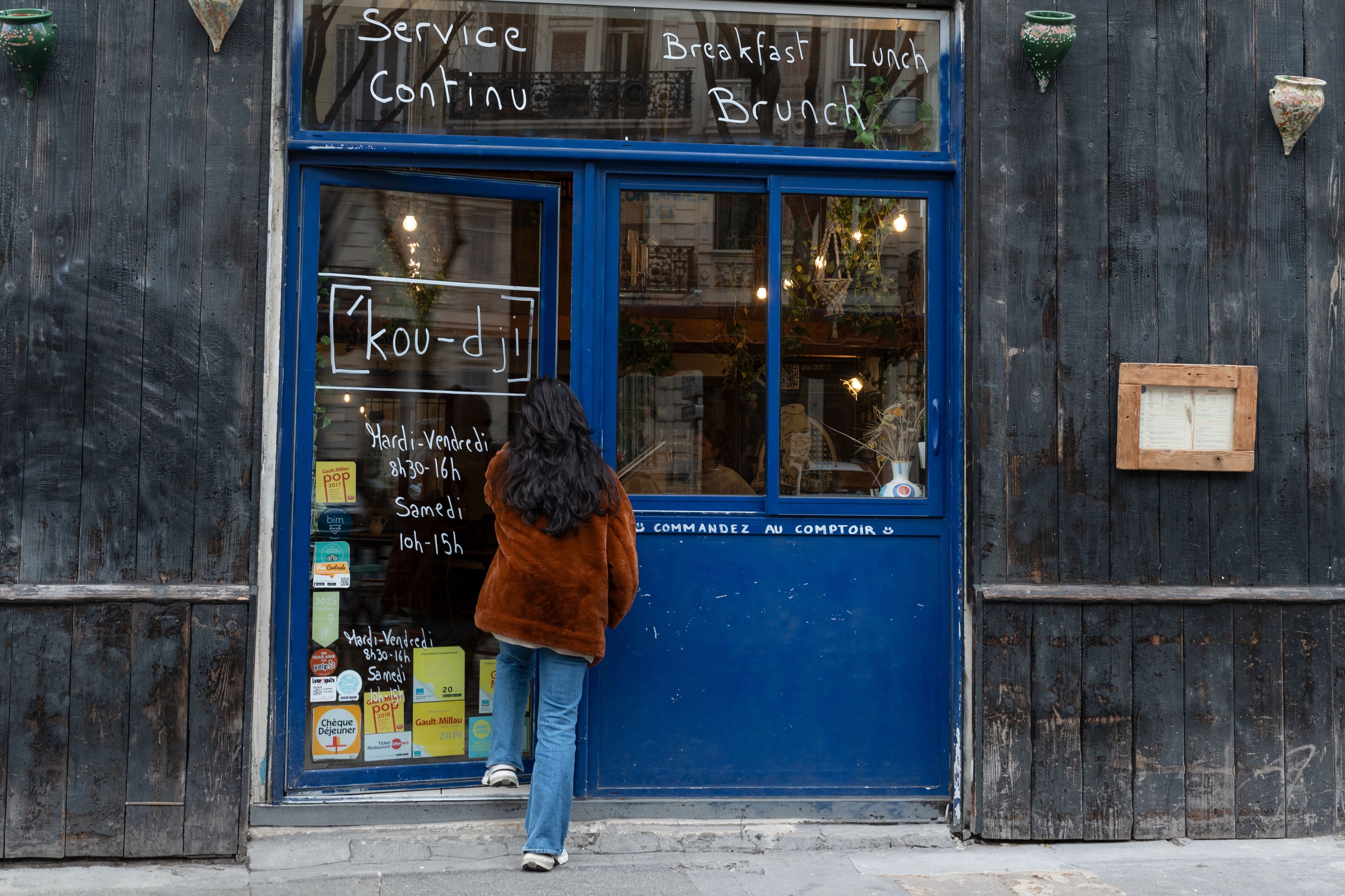 Eine Person steht vor dem Café Coogee in Marseille, betrachtet die Kreidetafel mit den Öffnungszeiten und dem Angebot für kontinuierlichen Service, Frühstück, Mittagessen und Brunch.