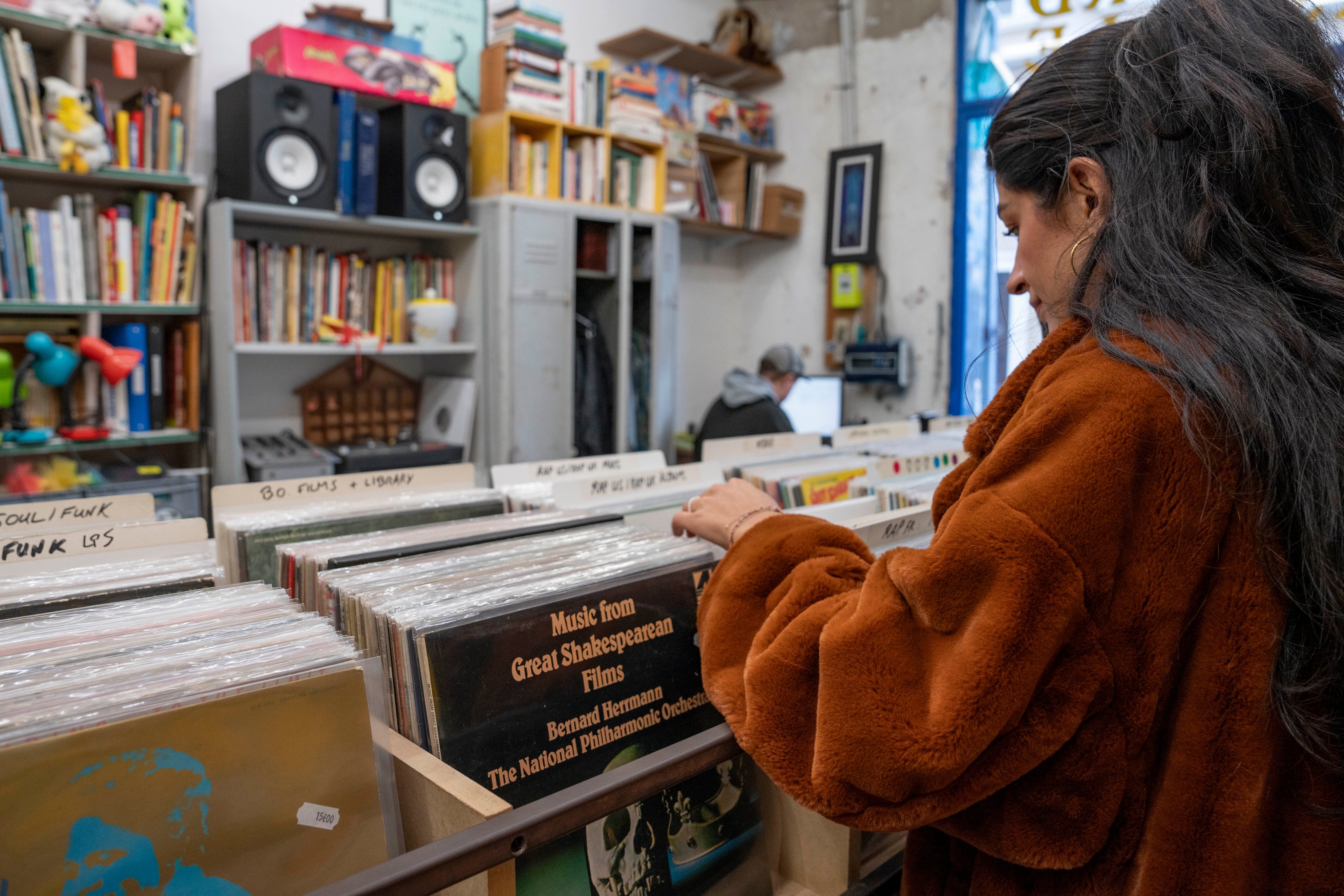 Eine Person durchsucht sorgfältig die Sammlung verschiedener Vinylplatten in einem kleinen, mit Büchern und Musik gefüllten Laden.