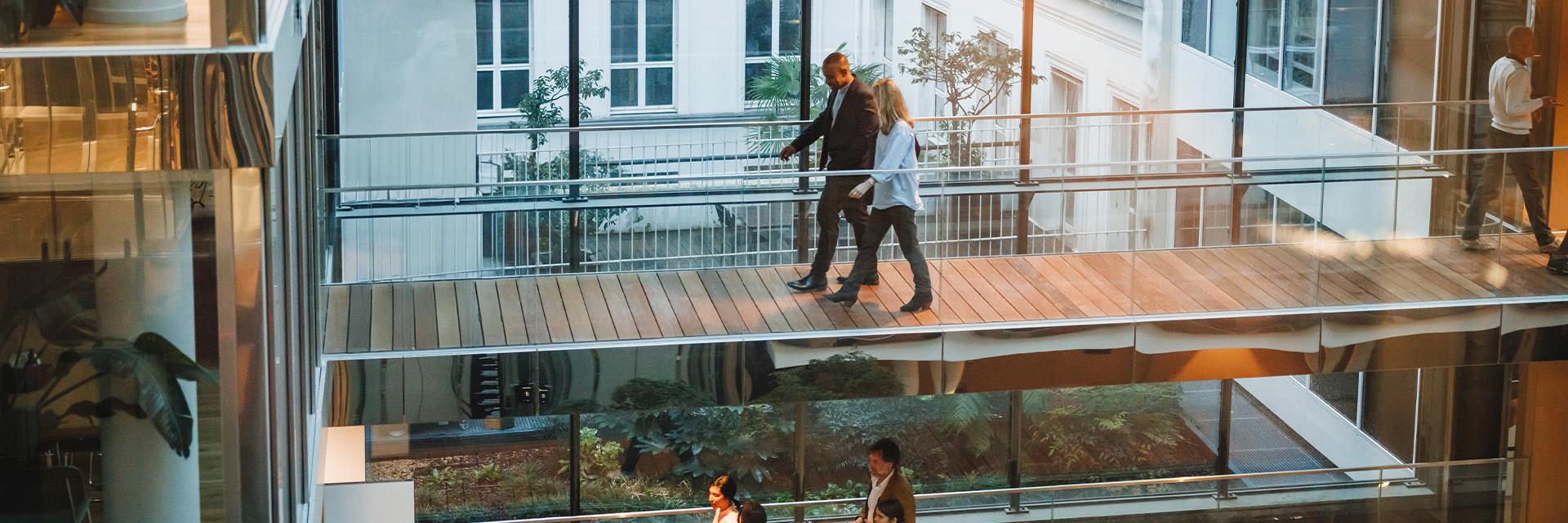 Two people walk across a wood walkway in a modern building.