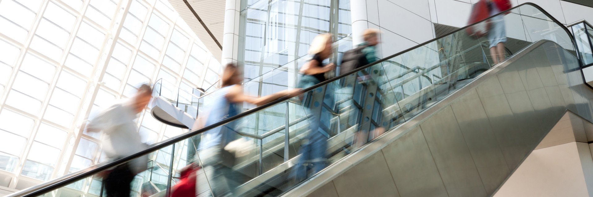 Several people ride up an escalator in a large, modern office building.
