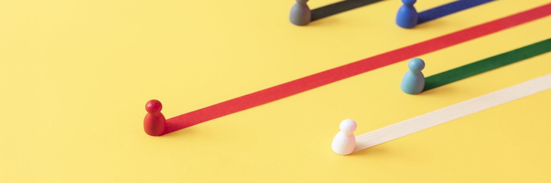 Wood game pieces site on pieces of ribbon, appearing to streak across a yellow background