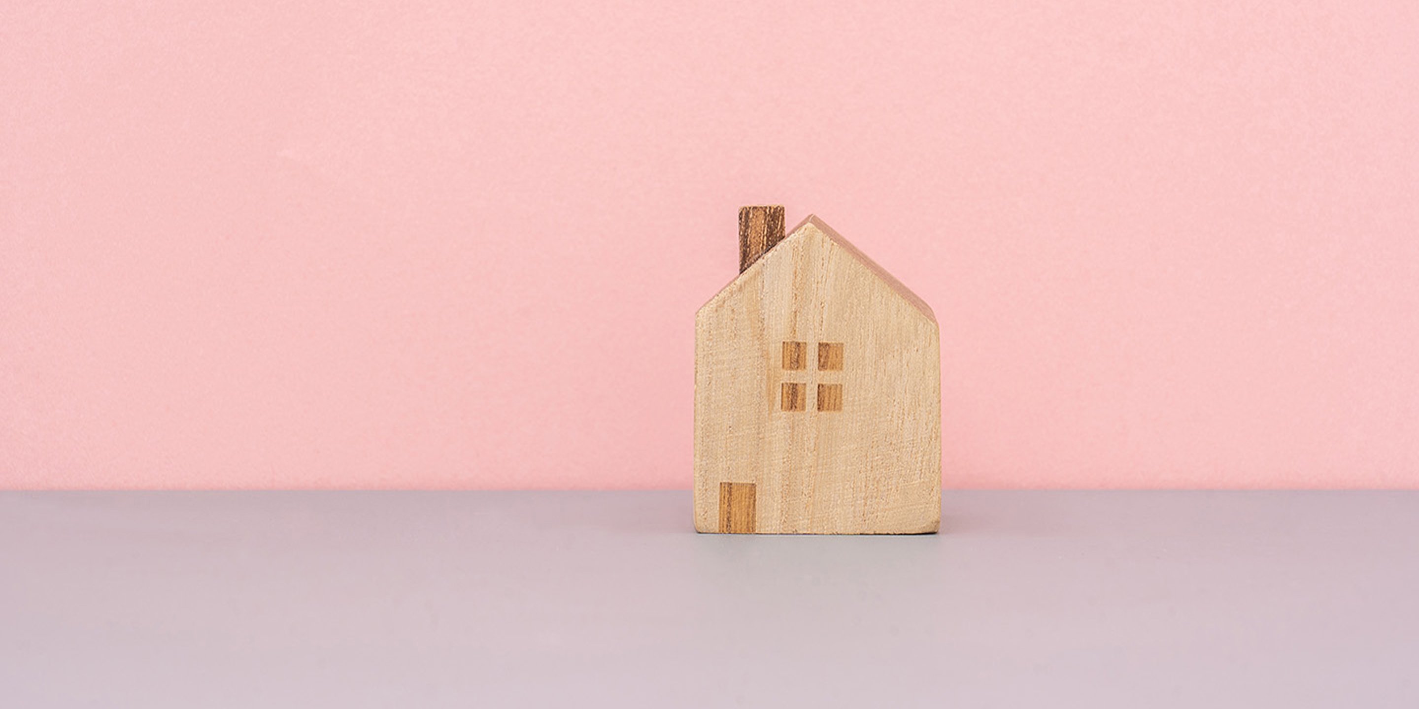 A wooden toy house on a pink background