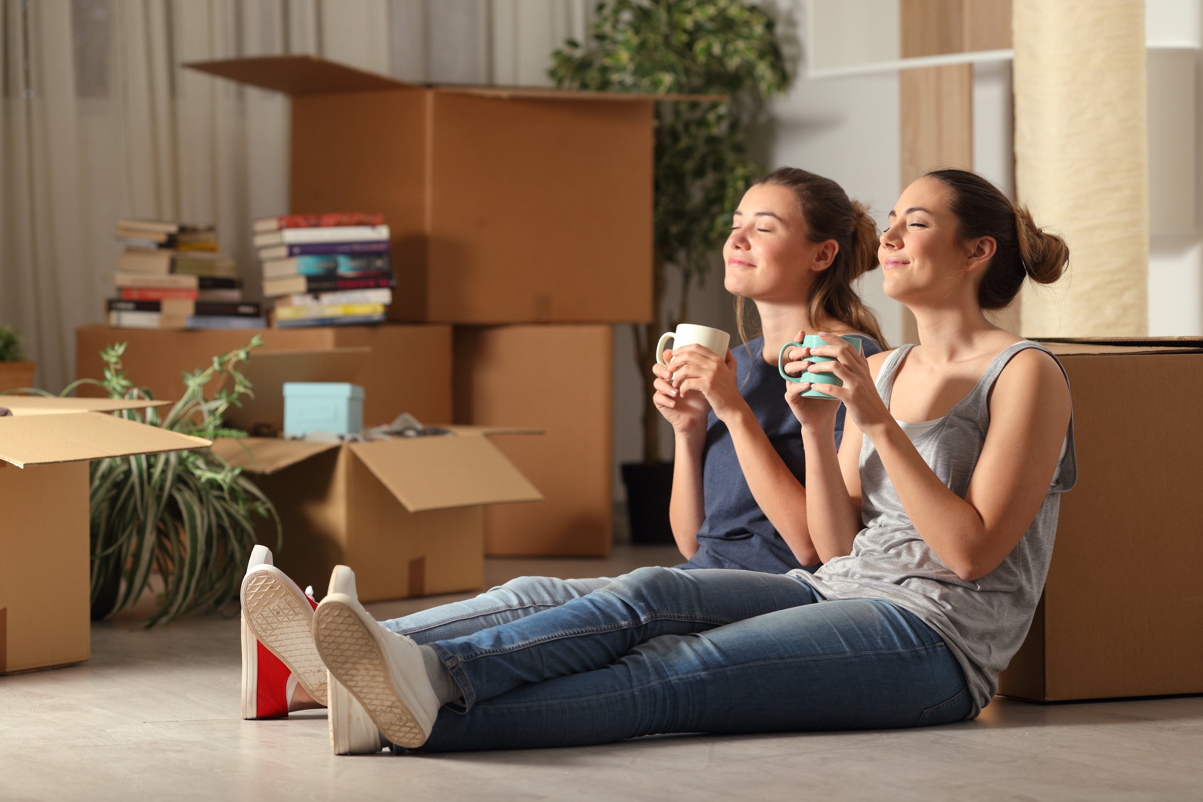 Couple sitting together drinking tea, surrounded by moving boxes.