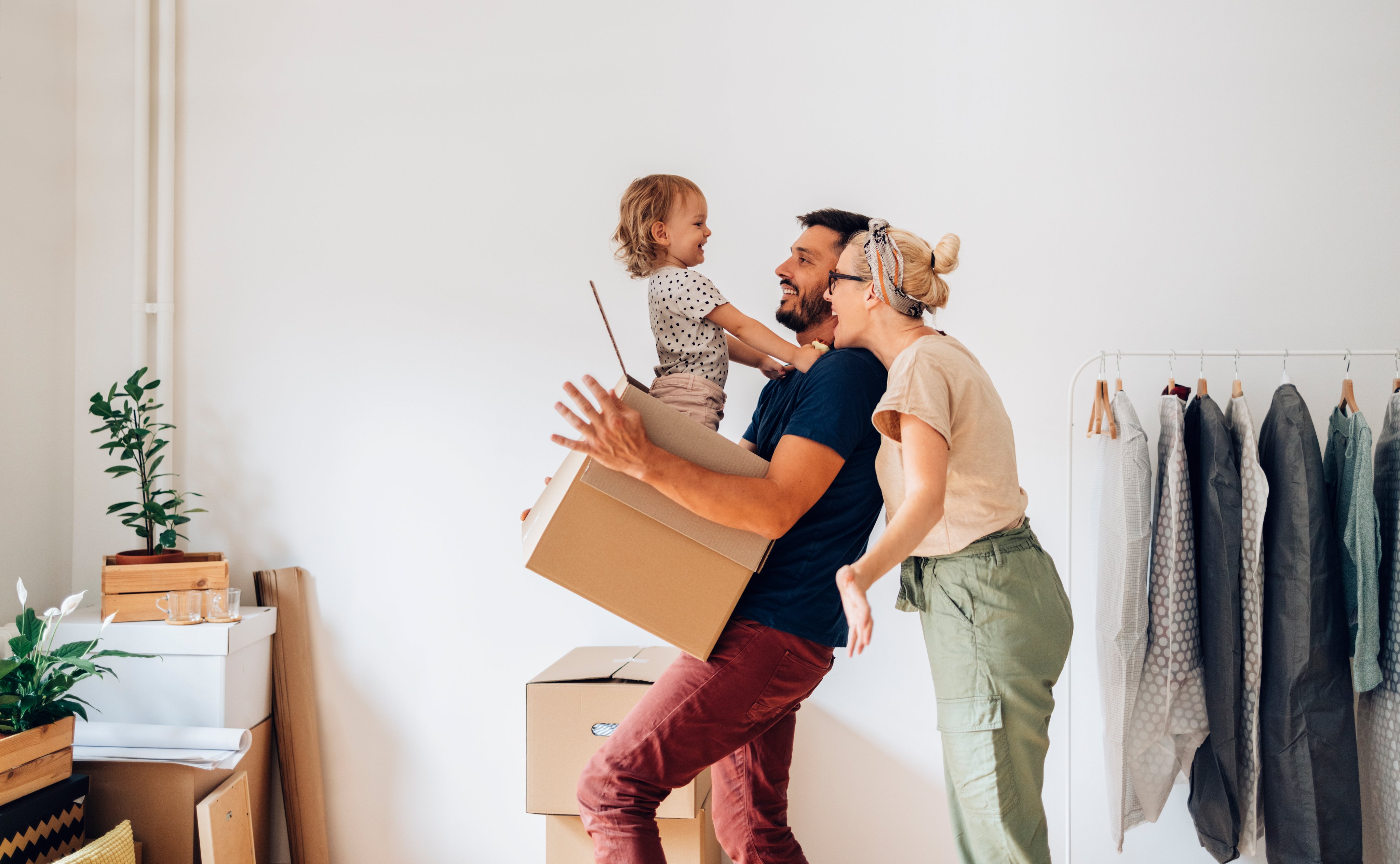 Dad holds daughter inside a moving box. Mum smiles. They are unpacking.