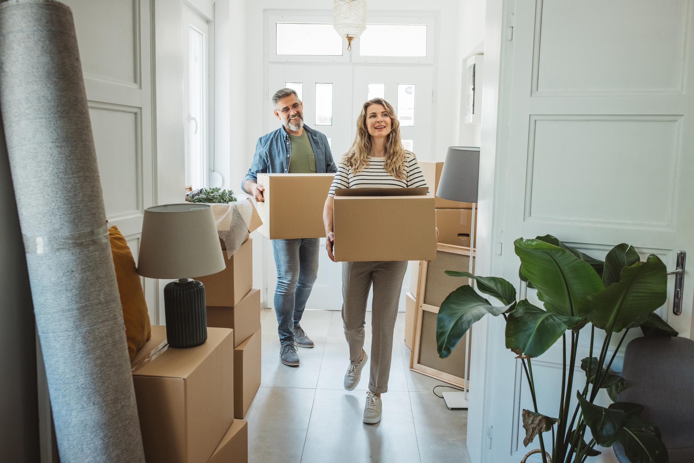 Older couple carrying moving boxes into their new home.