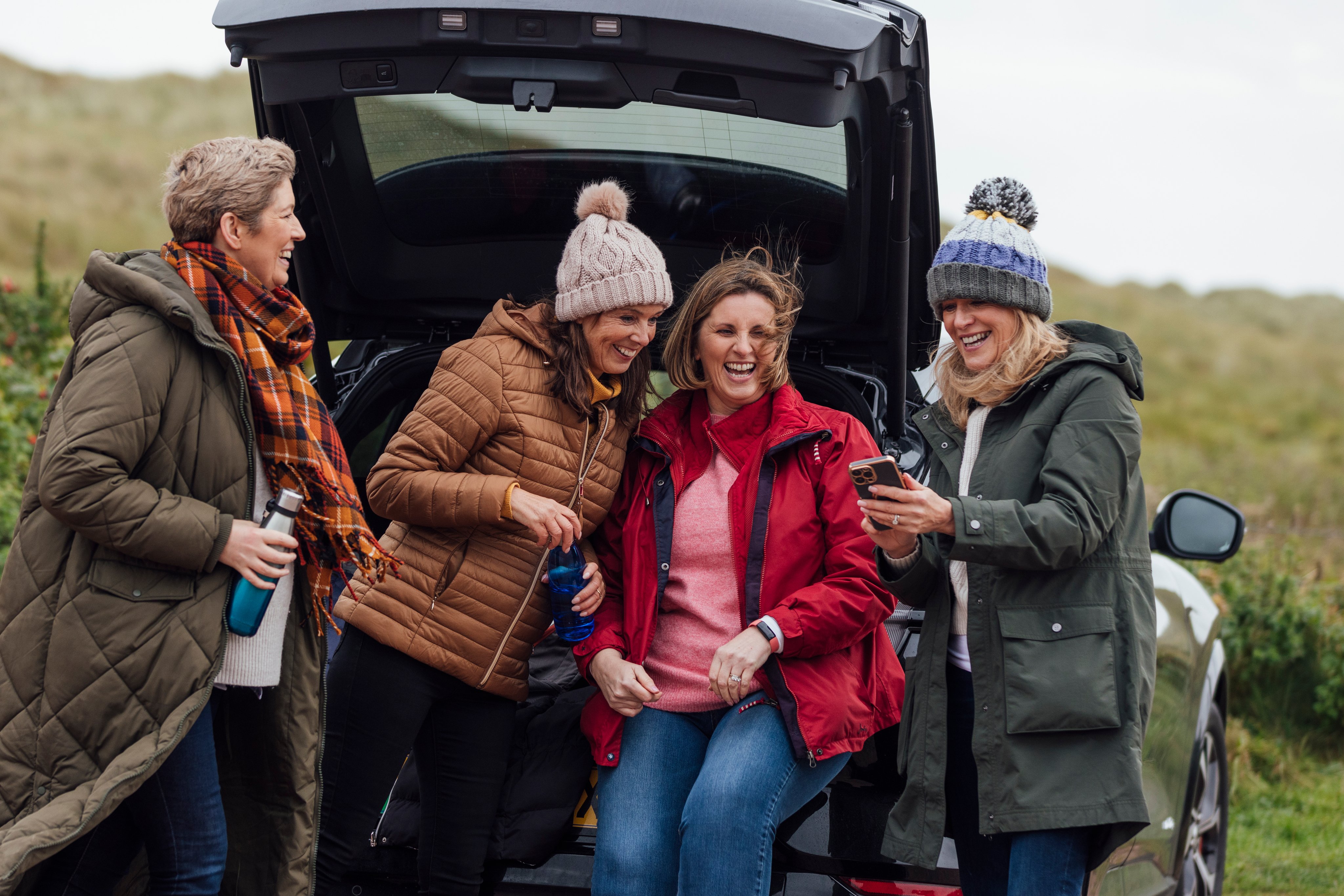 Four mature women in outdoor clothing prepare for day by sea at car