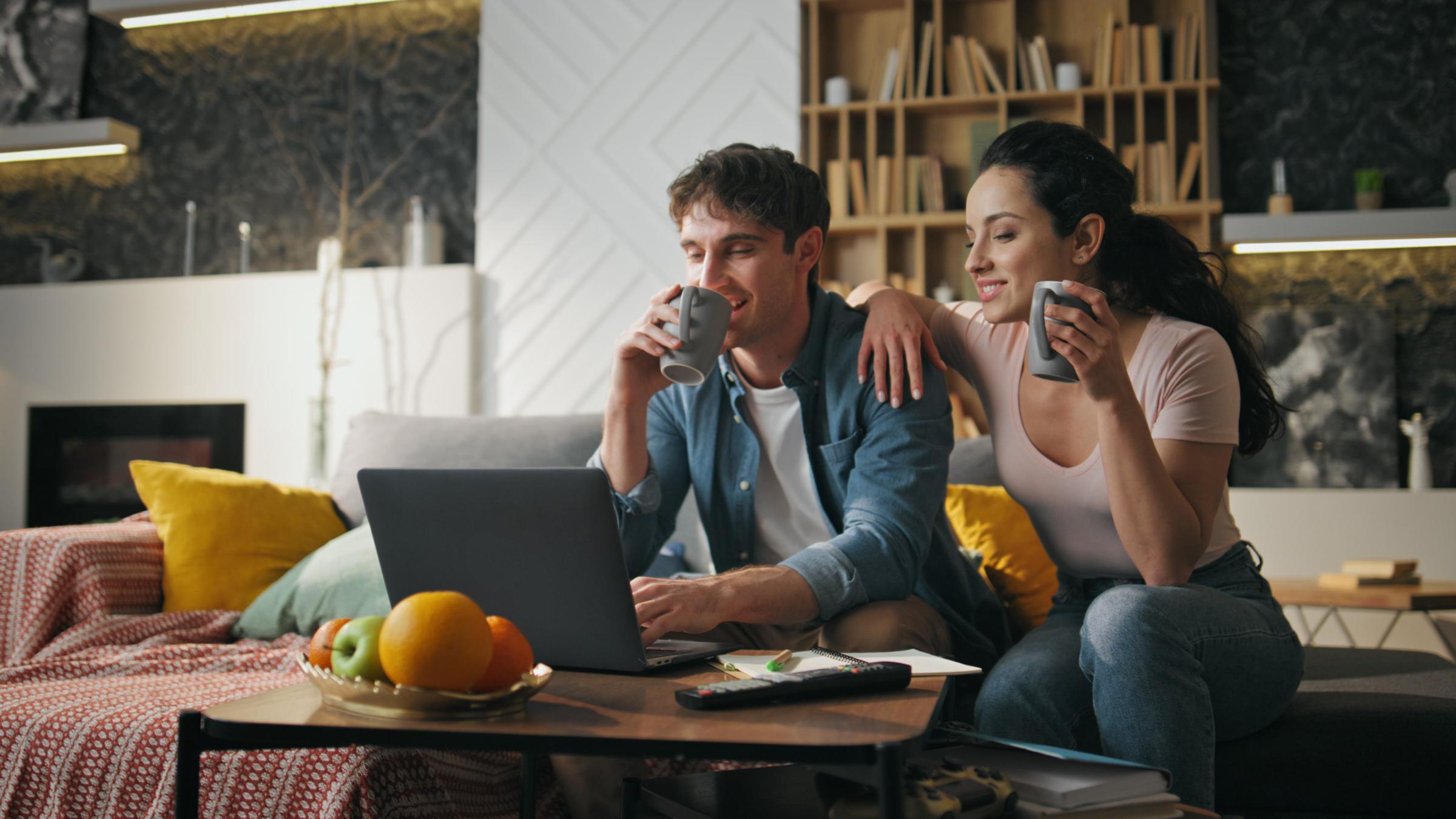 Couple drinking coffee at home living room looking on laptop