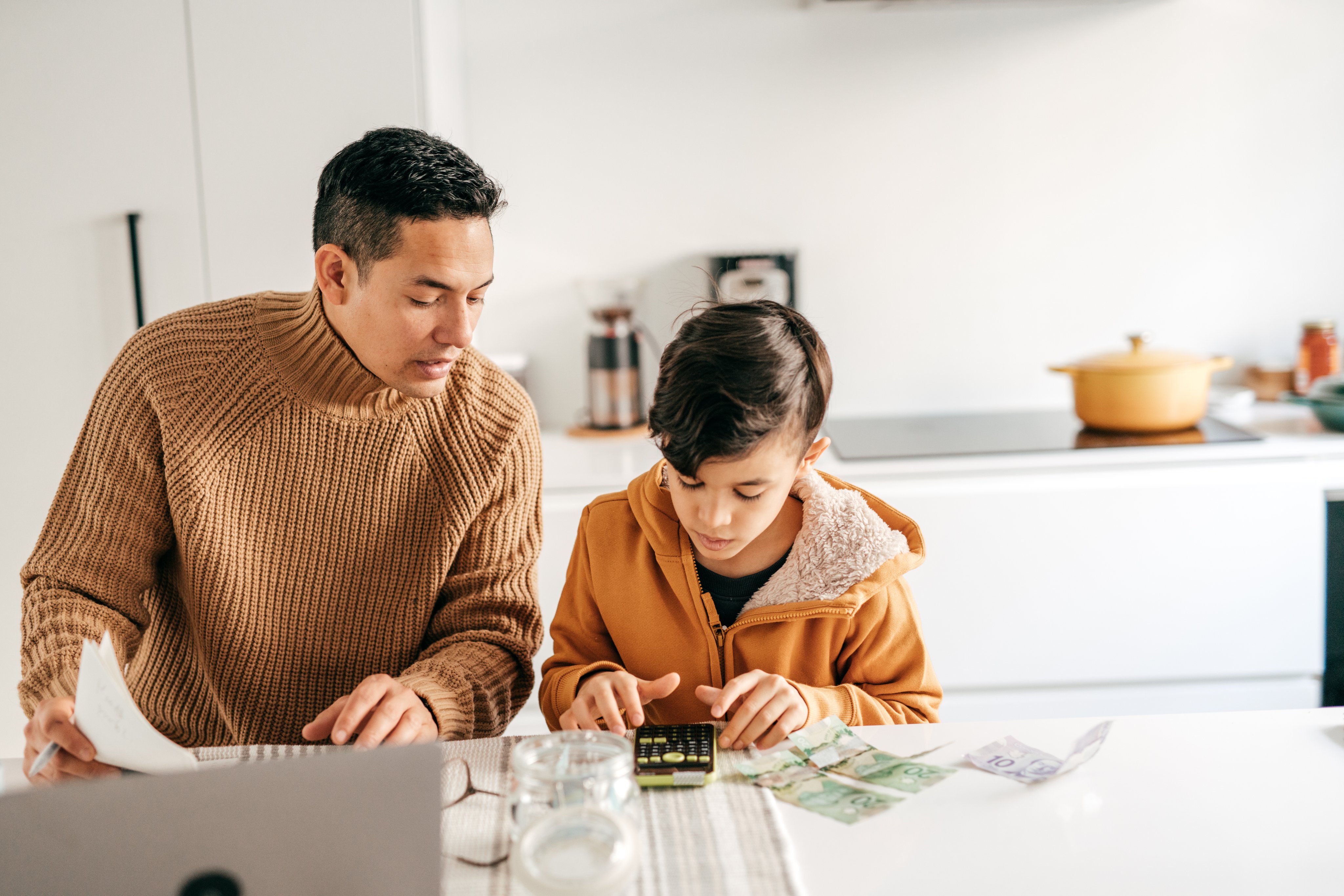 Father teaches son about finances while sitting in a kitchen