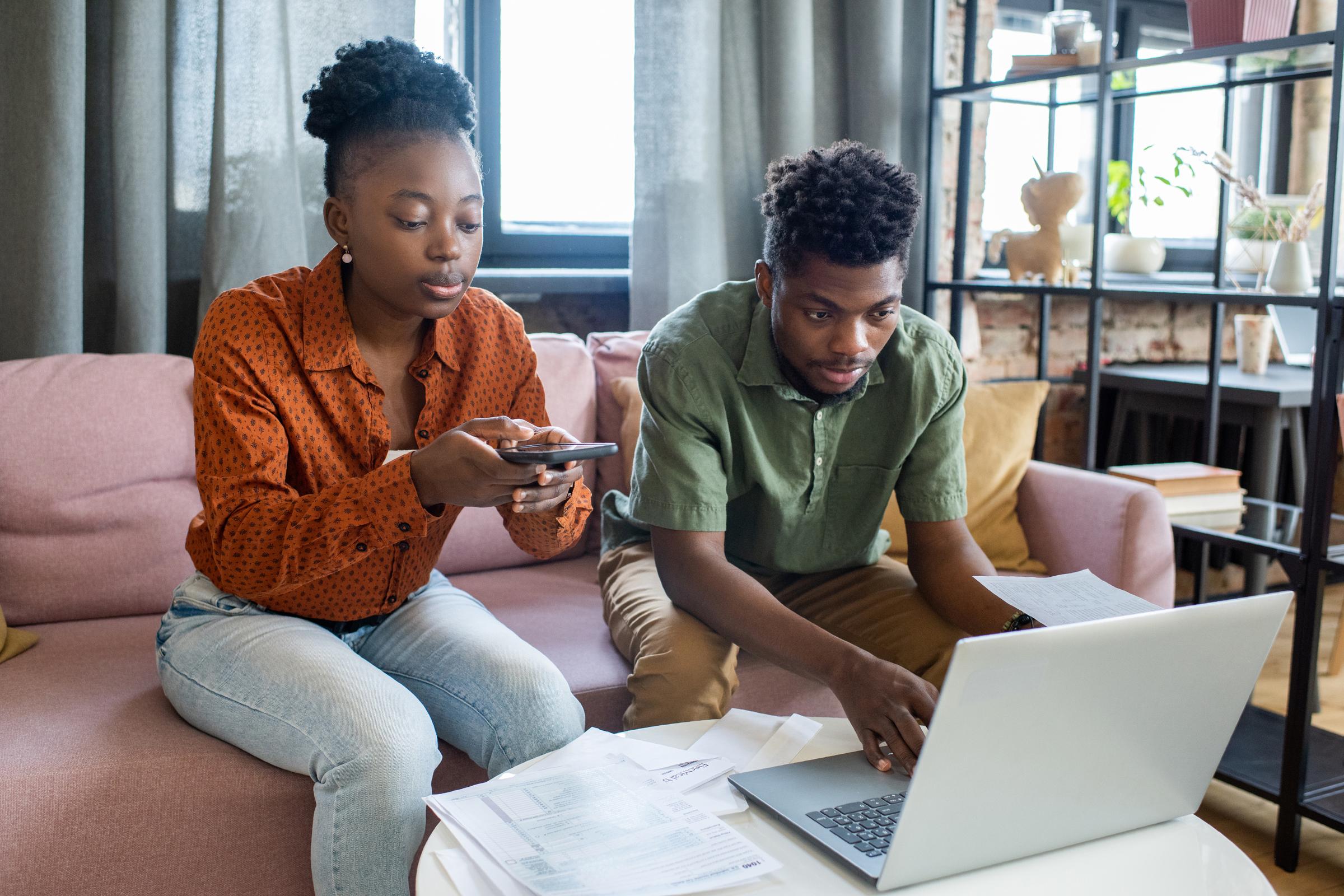 Couple sort tax papers while on mobile phone and laptop