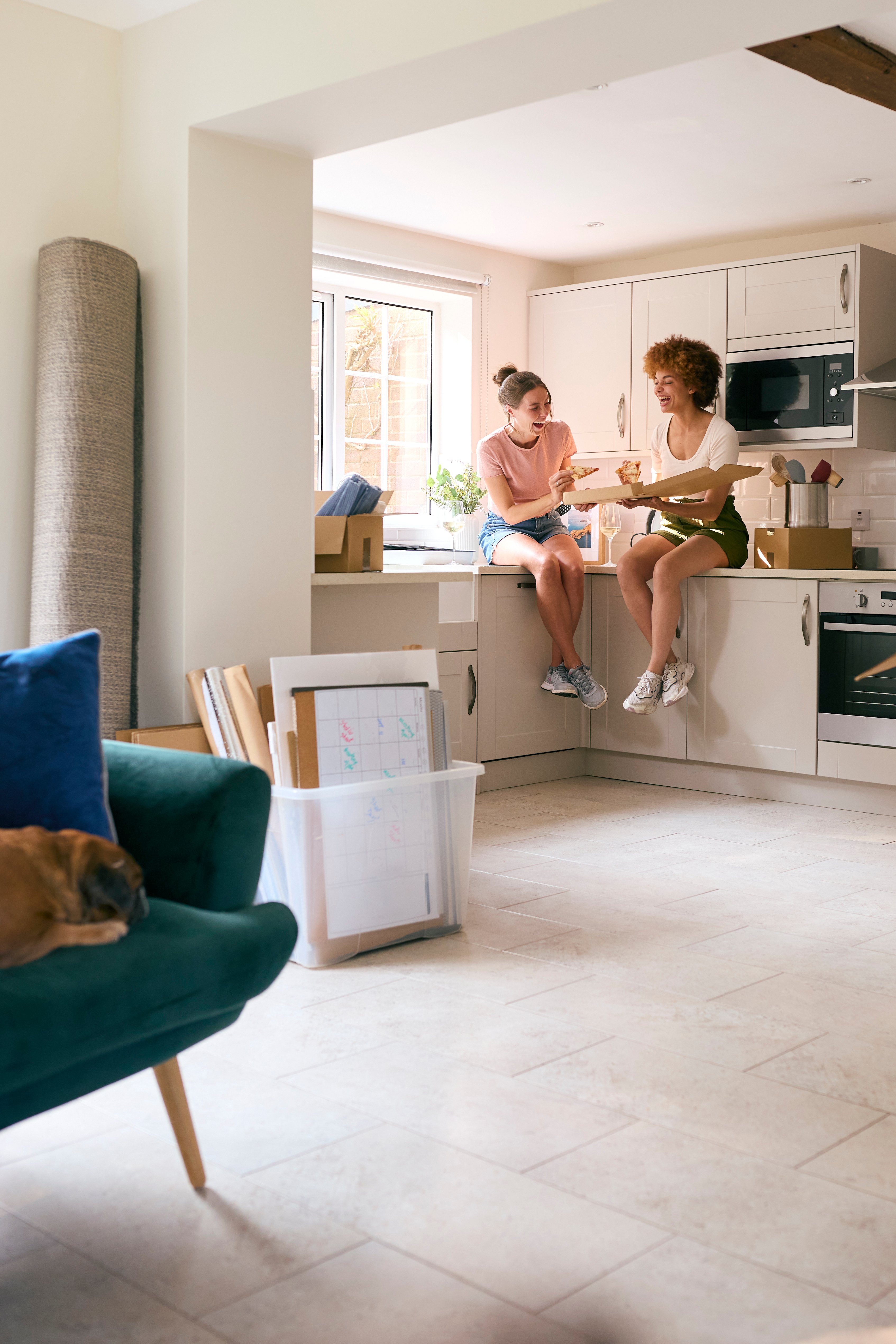 two young women share a takeaway pizza in their new home