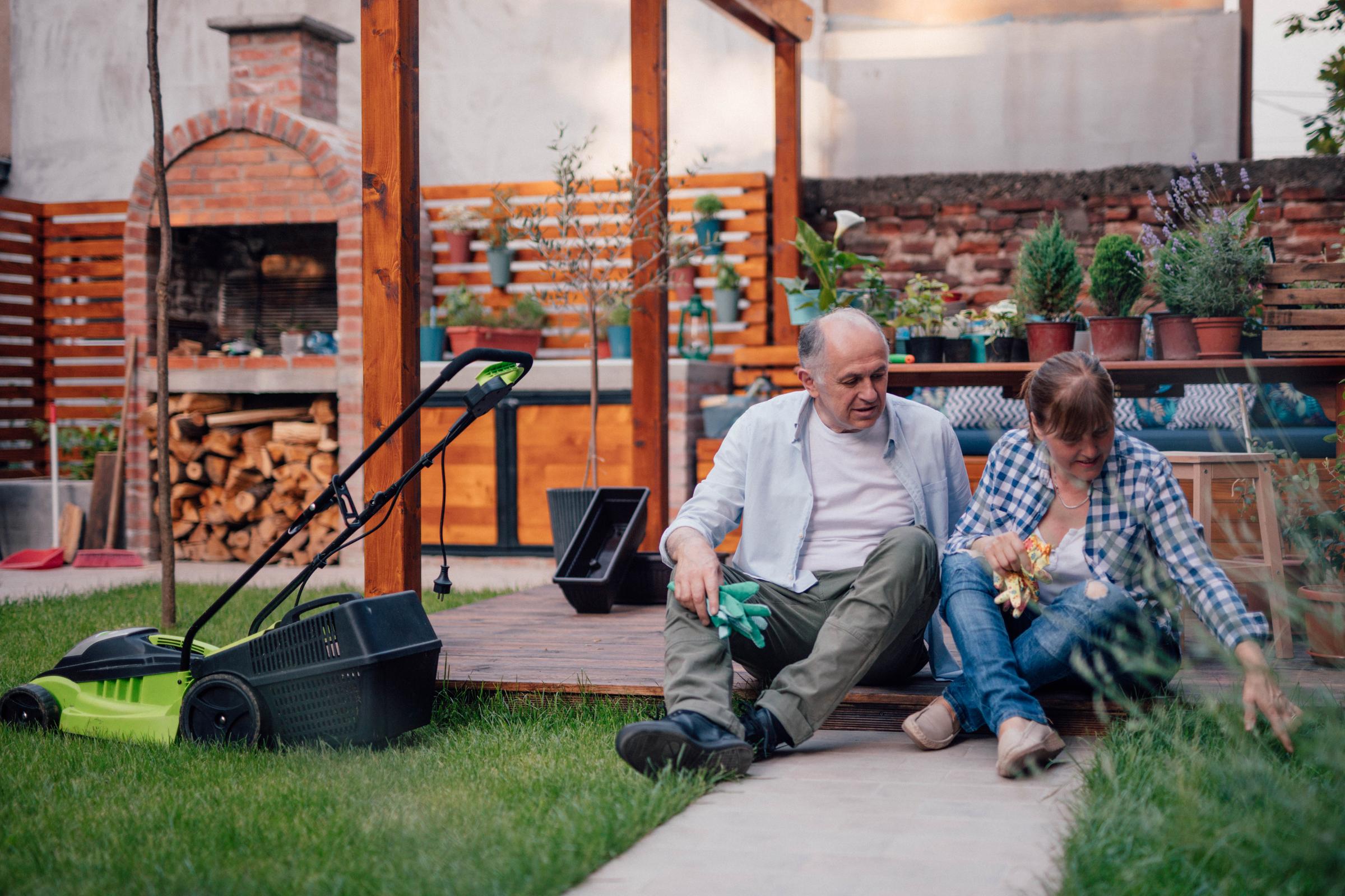 A mature couple sit in their garden. They are looking at their grass. 