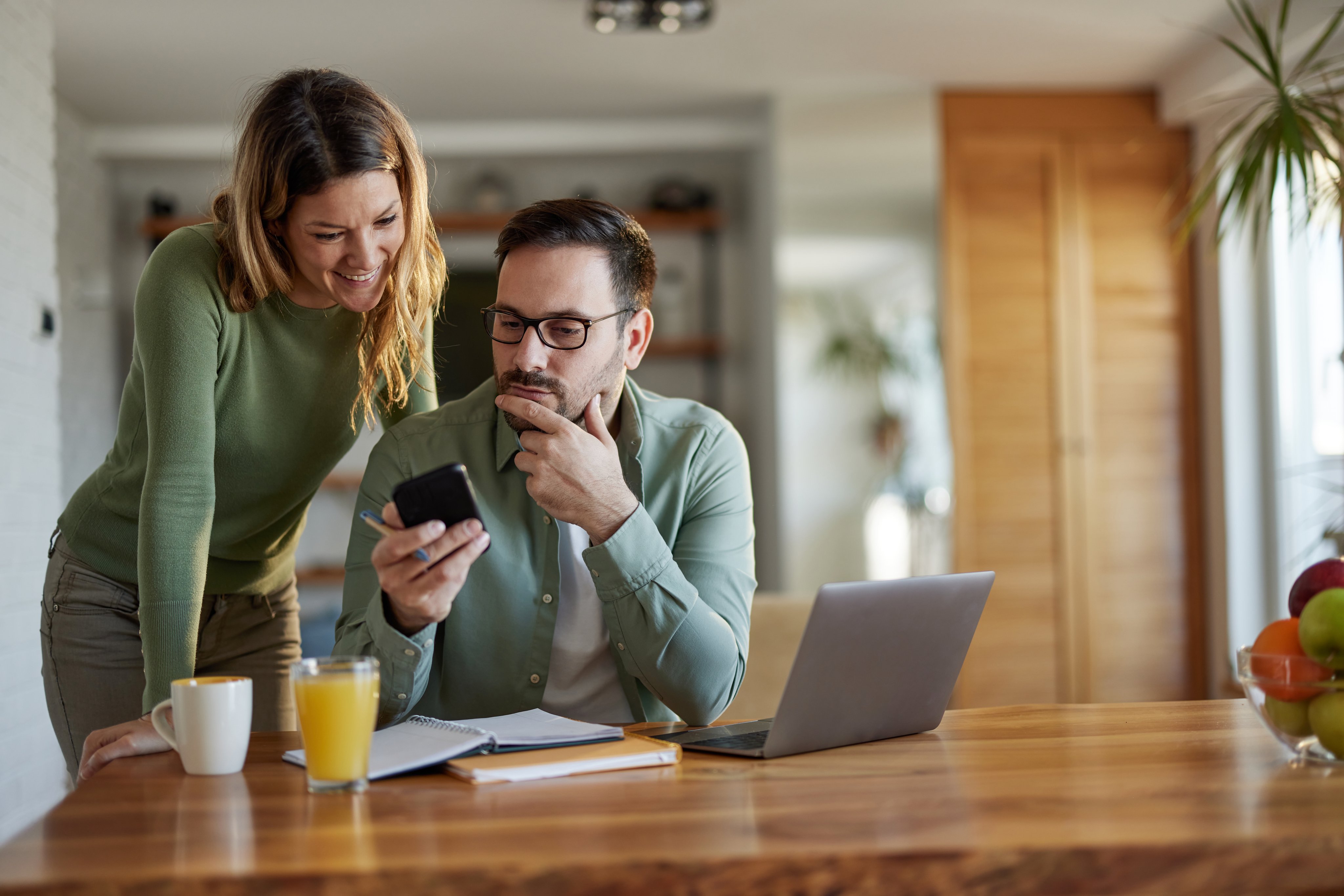 Young couple reading a text message on smart phone while working at home.