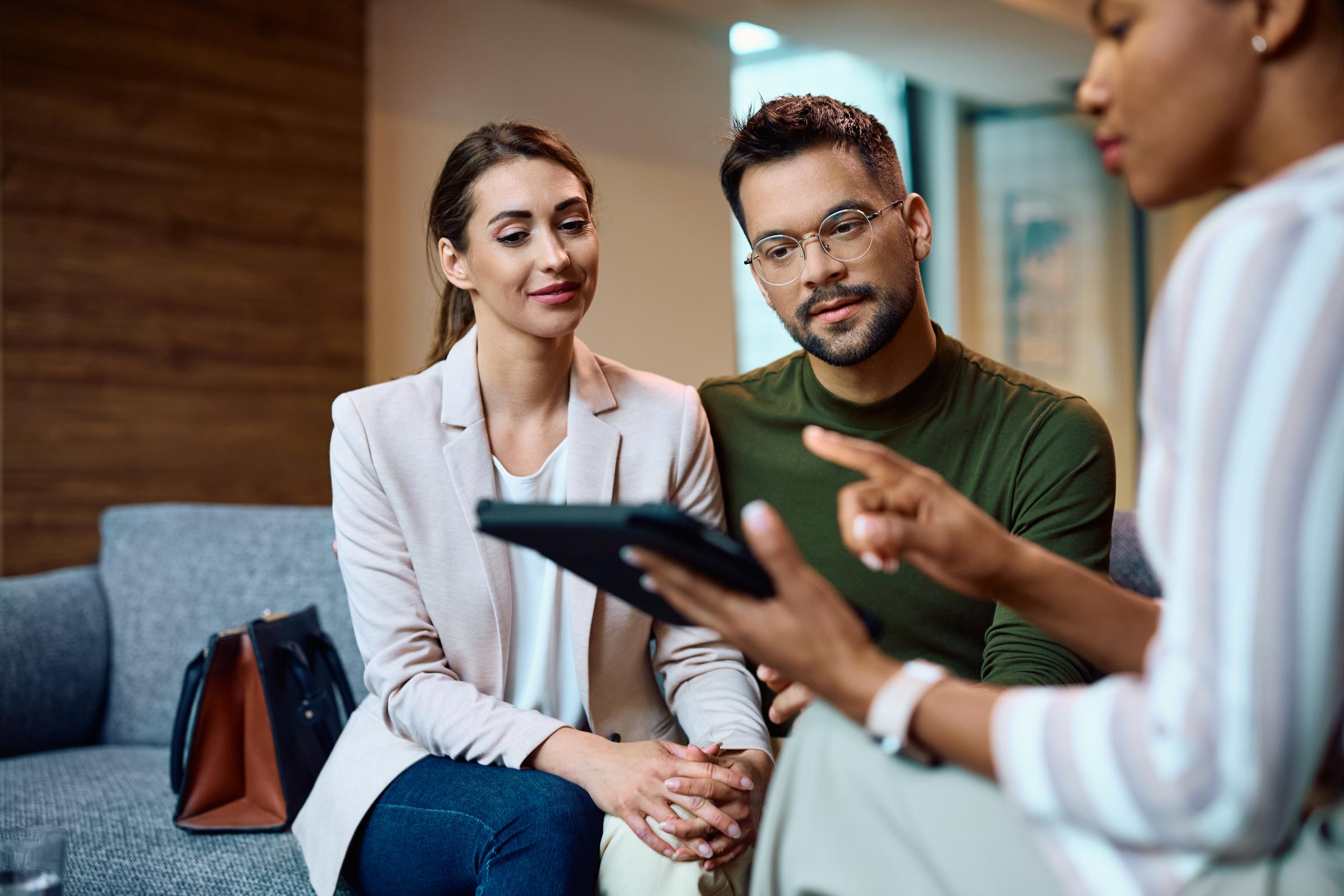 Young couple listening their financial advisor who is using touchpad during a meeting in the office.