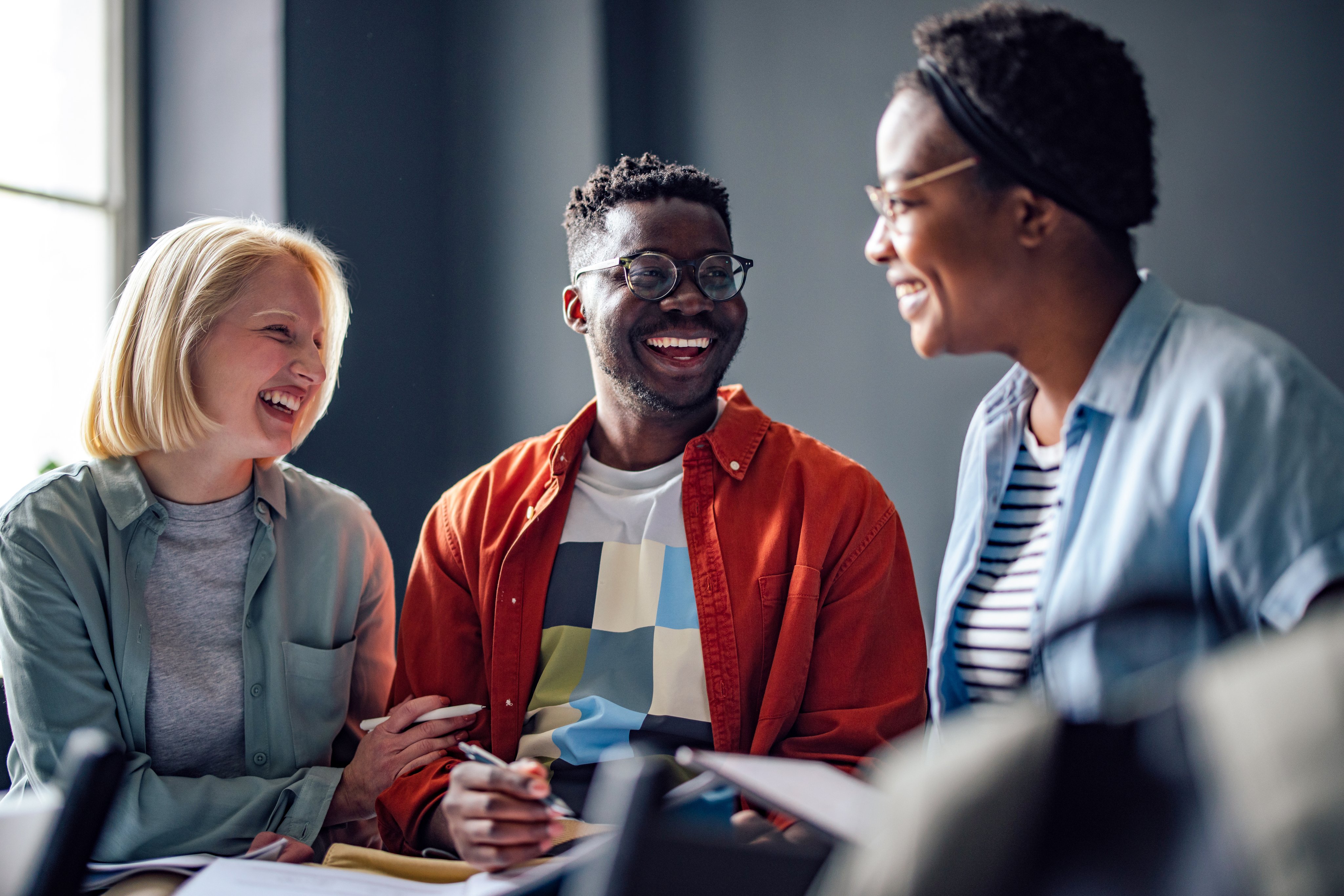 A man and 2 women sit together, smiling. They hold pens and a notepad.