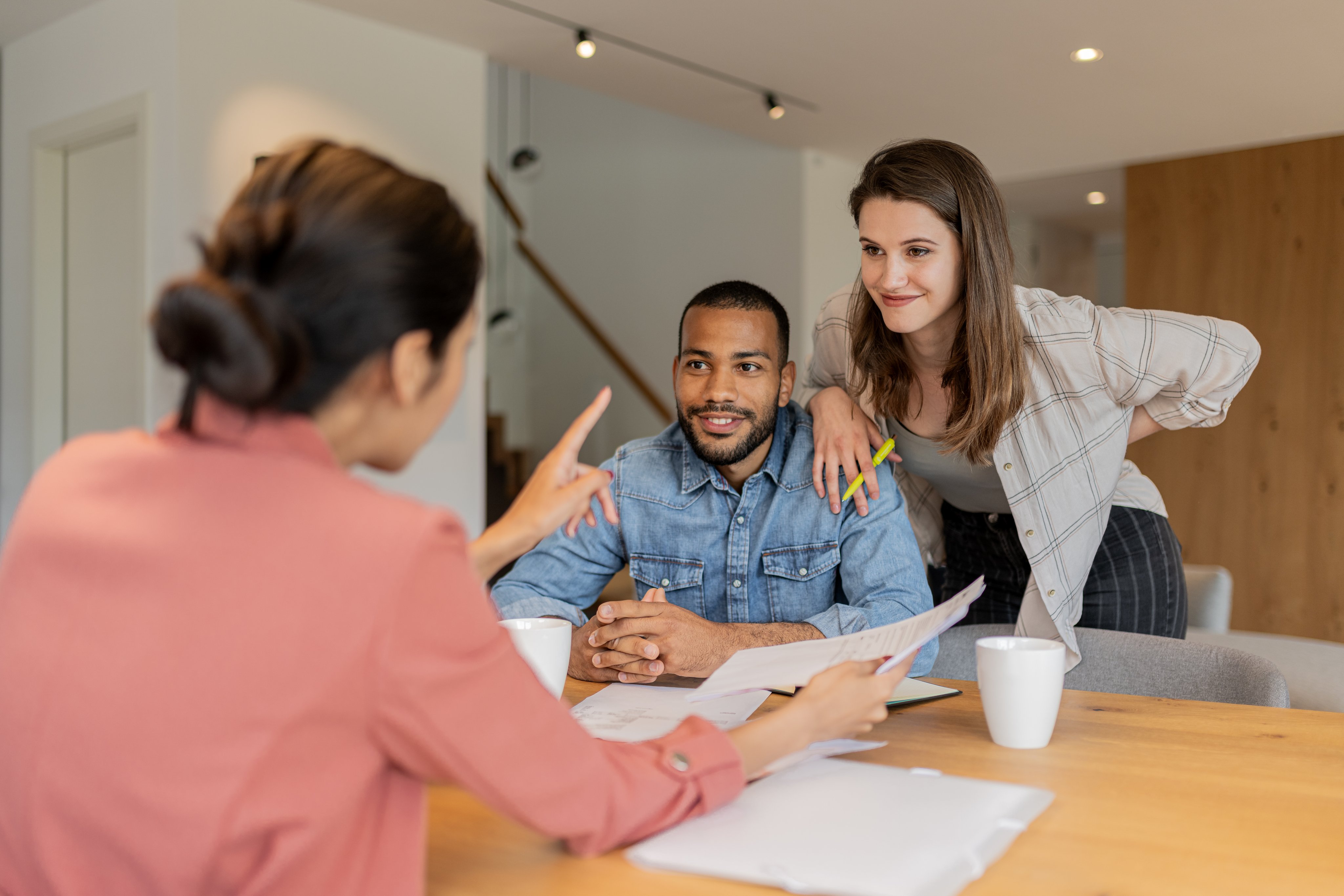 A financial advisor advises a multiracial couple in their apartment about financial investment,