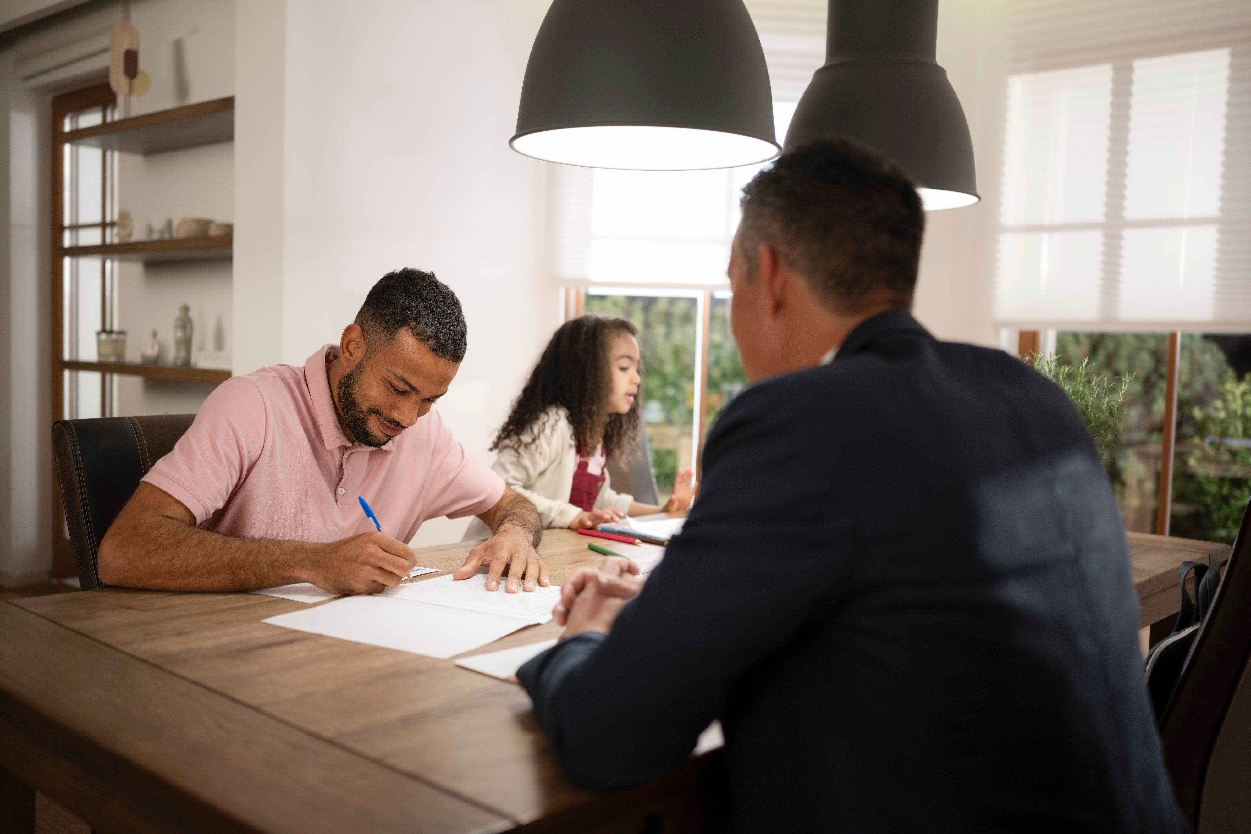 Male client signing documents with insurance agent as they sit at dining table