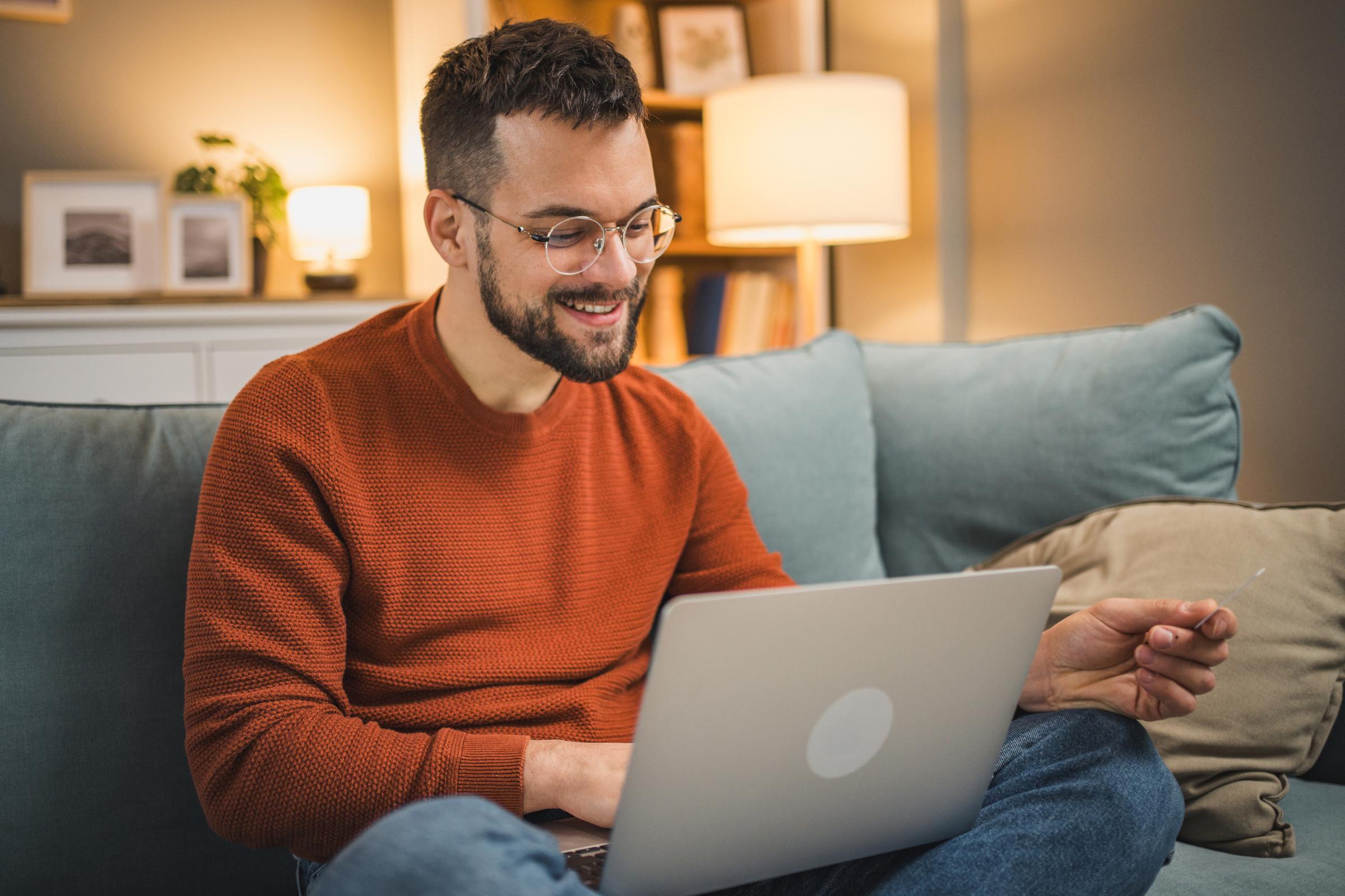 Man smiling while looking at credit card and using laptop