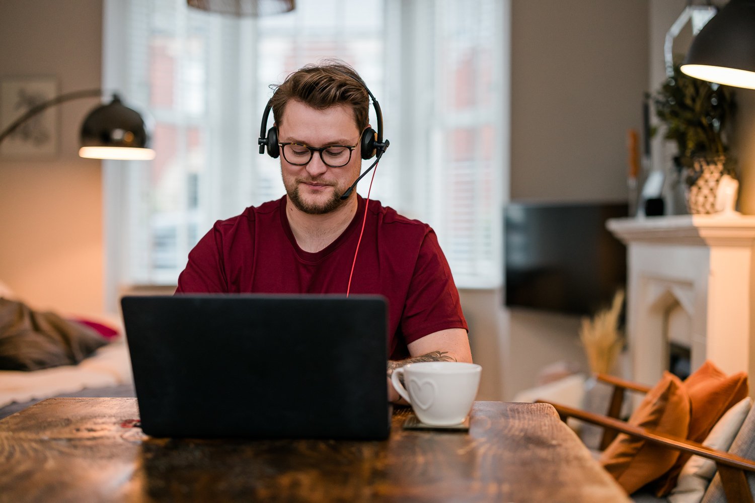 Man sits at desk wearing headphones working on his laptop. 