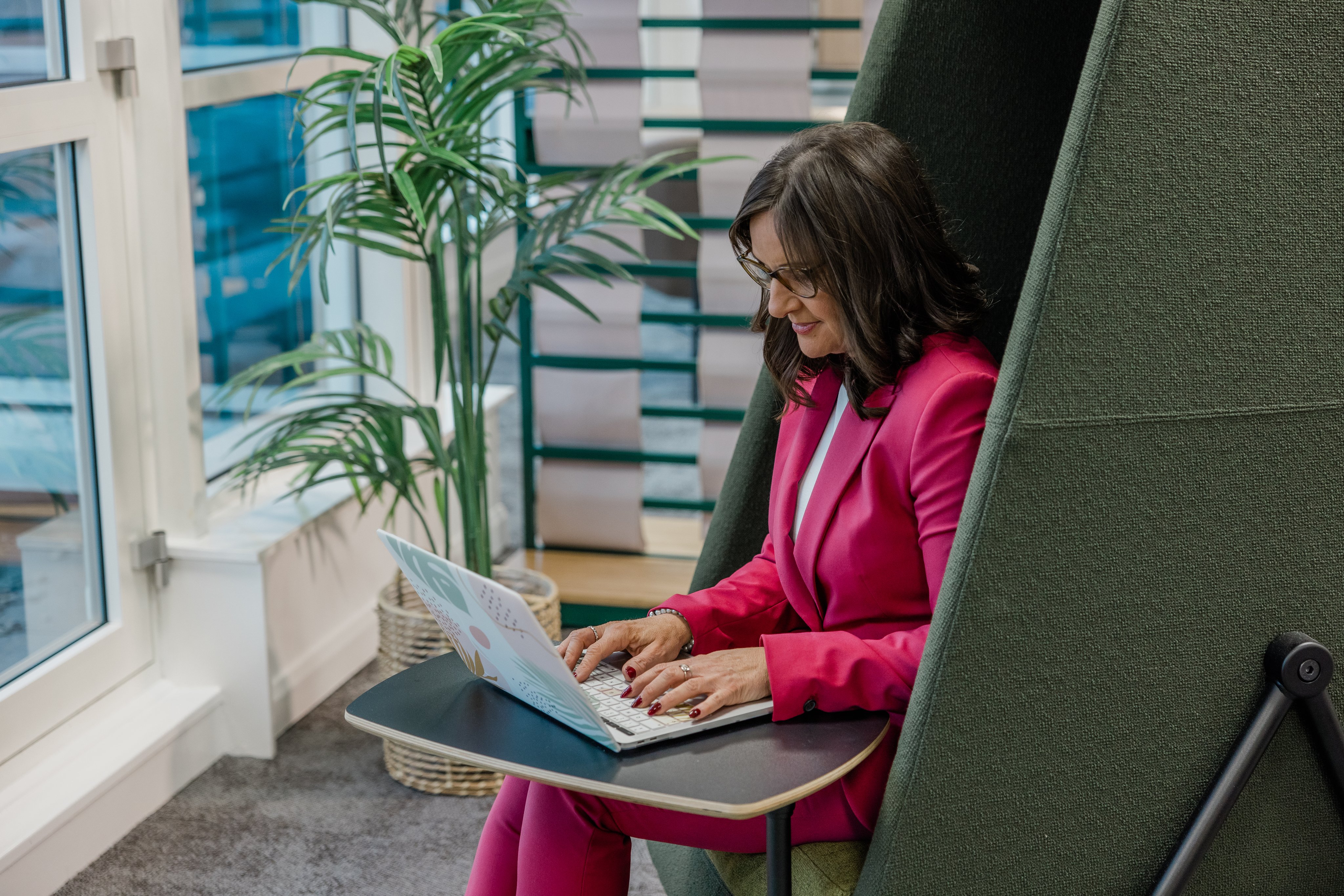 Woman in a pink suit works on laptop in office