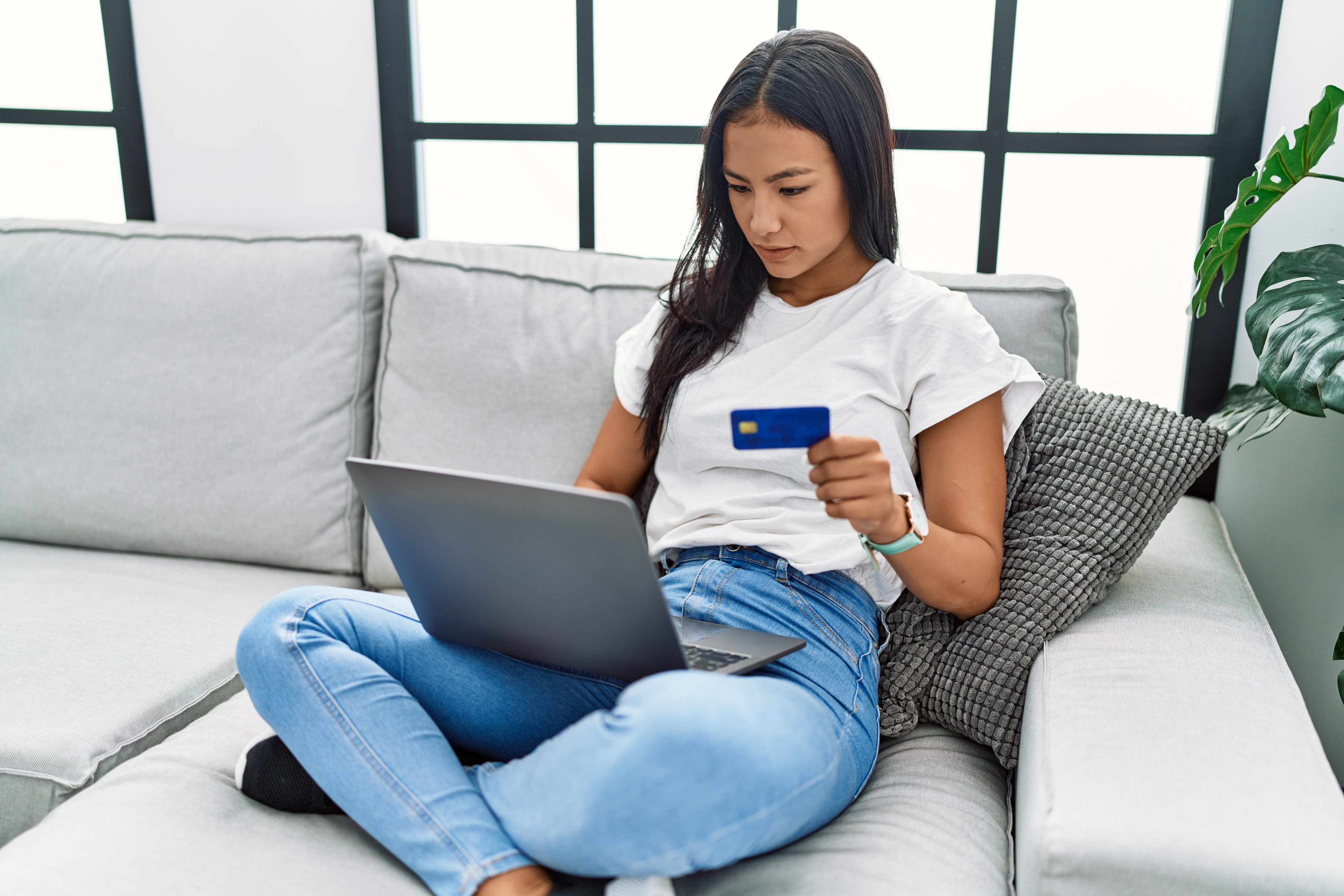 Woman using laptop holding credit card at home