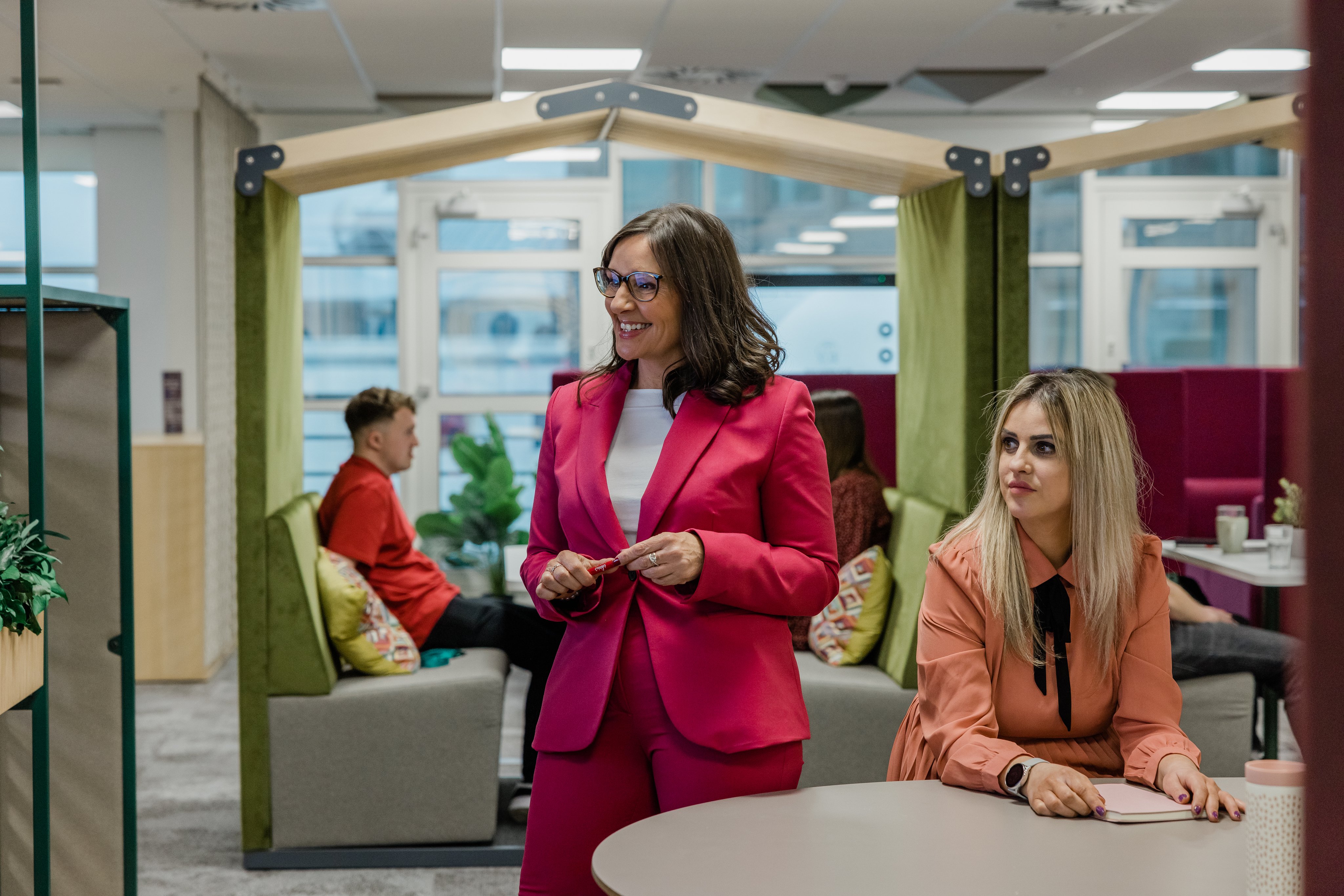 A woman in a suit stands smiling in an office 