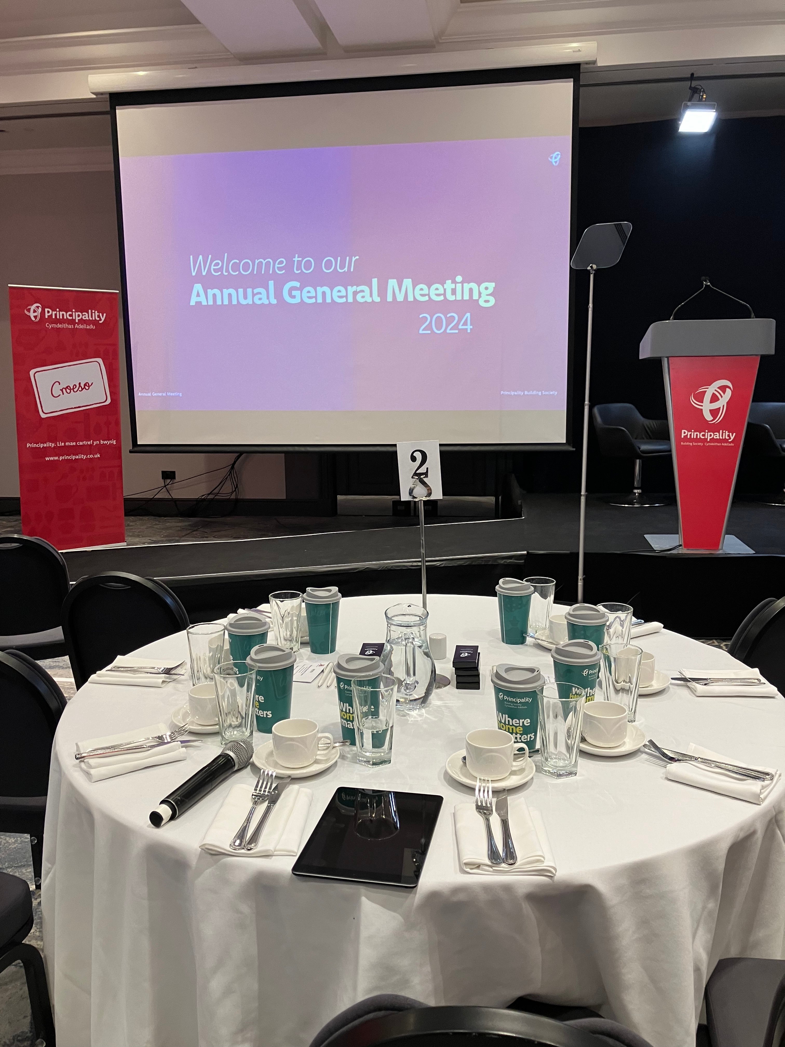 A screen in front of the table "Welcome to our Annual General Meeting 2024"