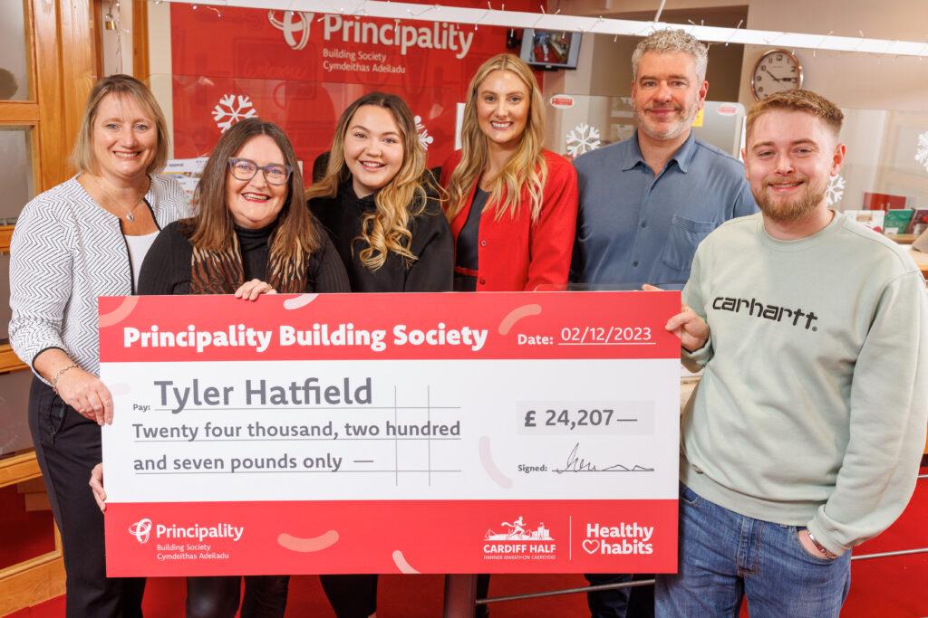 Tyler Hatfield holding a check for £24,207 from Principality Building Society