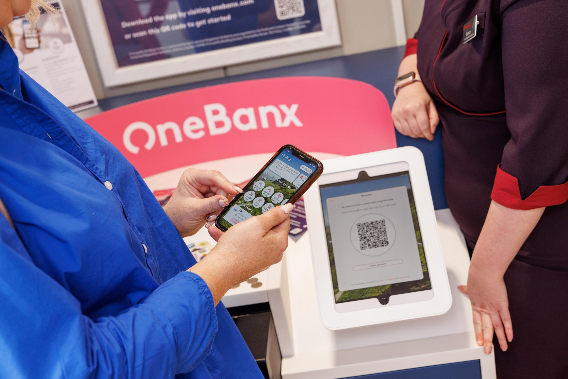 Woman using OneBanx app and being assisted by a Principality Customer Consultant to  deposit money using the OneBanx machine.