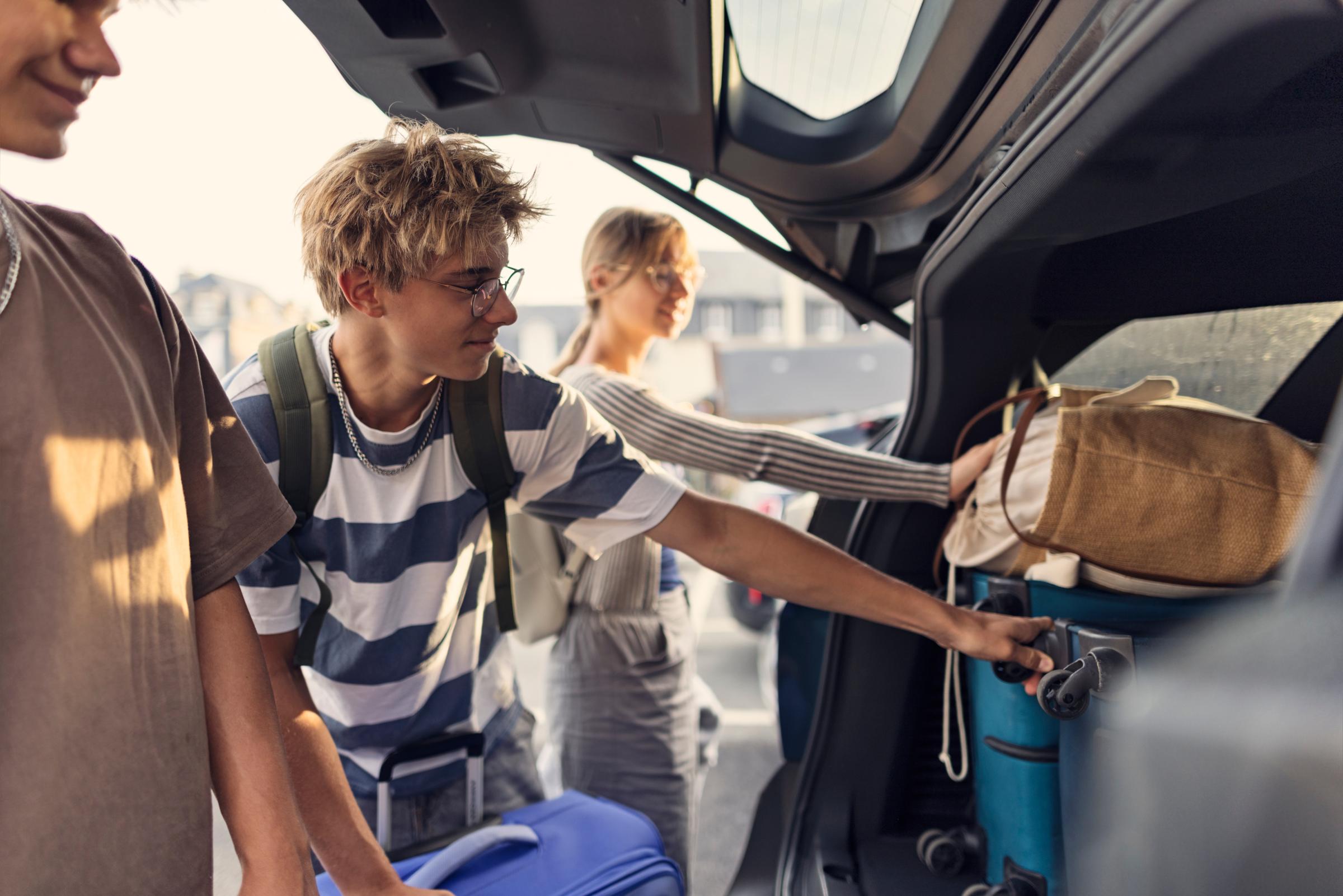 Teenagers helping to pack the family car for road trip. 