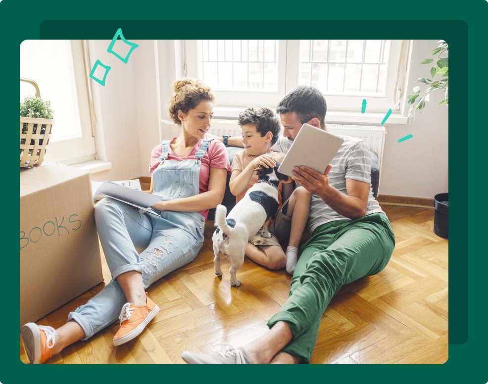 A mum, dad, and son sit on the floor with their dog, They have a cardboard box labeled books next to them. 