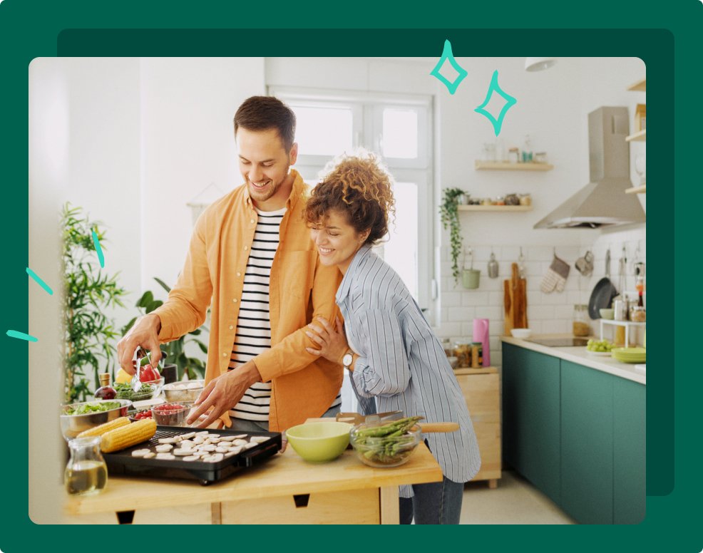 A couple are in their kitchen adding vegetables to a grill and preparing other food for a meal. 