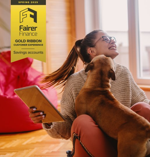 Woman sitting on the floor and playing with dog. In hand tablet. Living room interior. Fairer Finance Gold Ribbon in the top left corner of the image for savings customer experience.