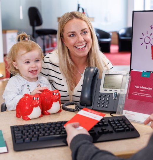 Woman and child have conversation at desk with customer consultant in prinipality branch