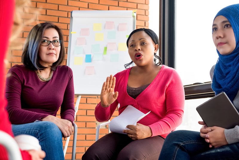 Three women participating in a training session, with a board behind them covered in post-it notes.