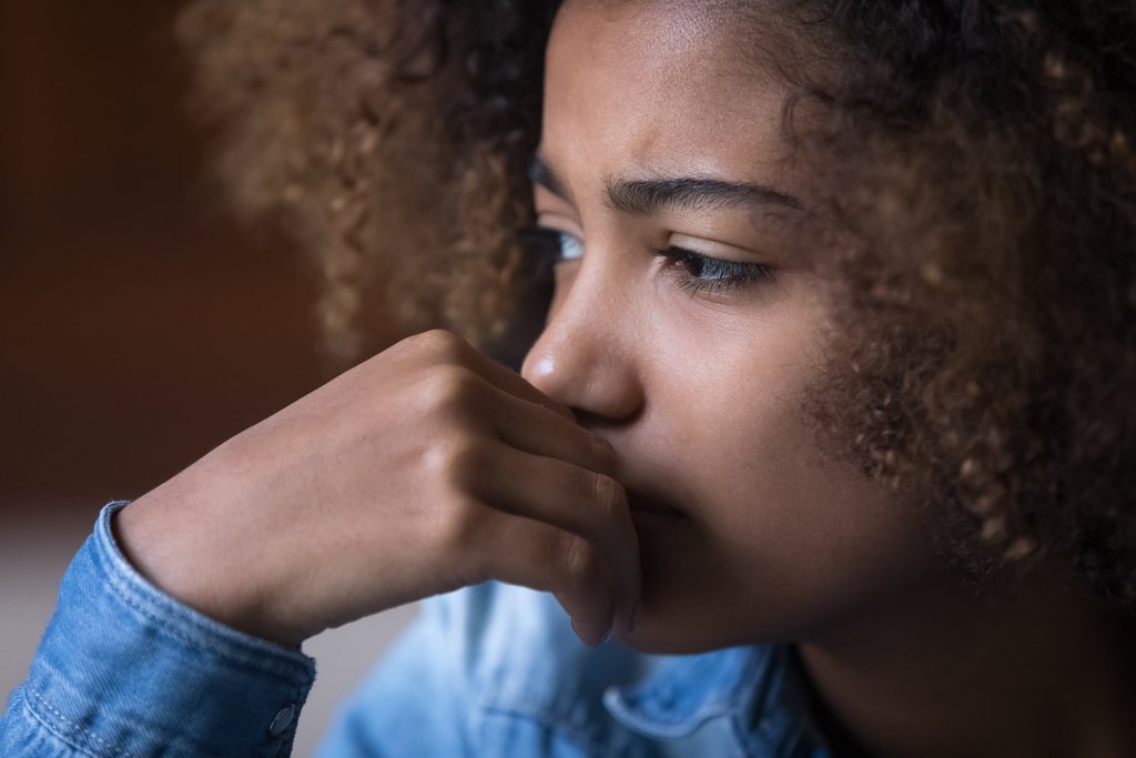 A close-up image of a young girl looking towards a window, facing away from the camera.