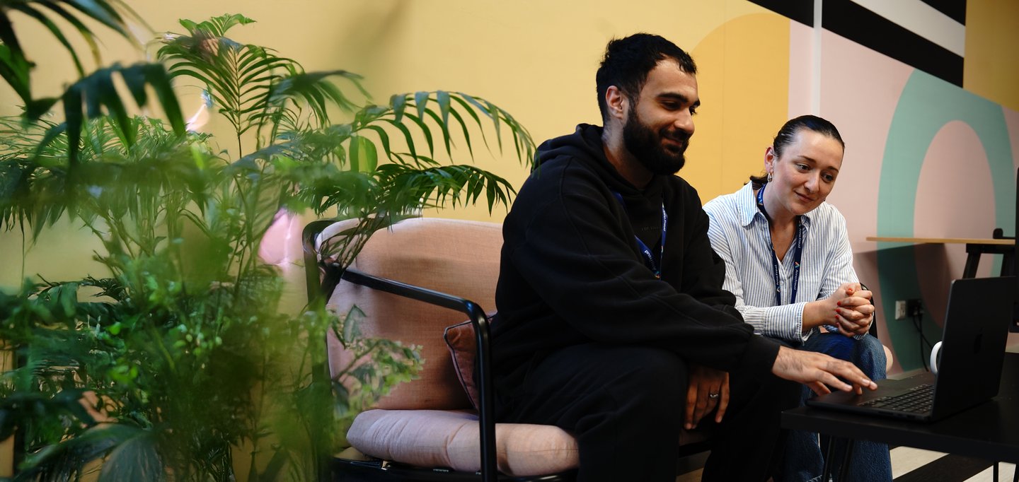 Two Anna Freud students, sitting together, looking at a laptop, smiling.