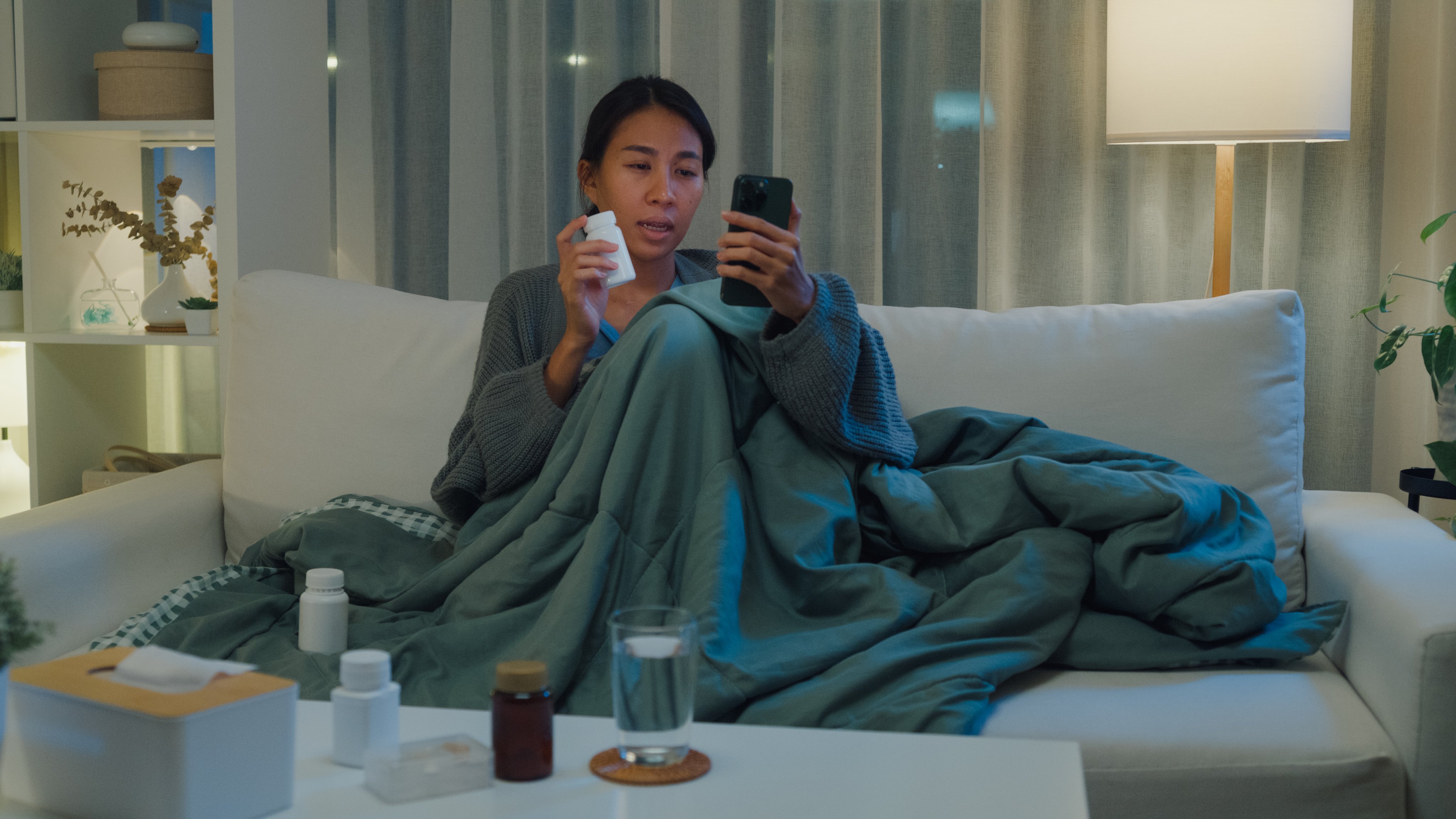 A young woman at home on the couch under a blanket looking at her phone