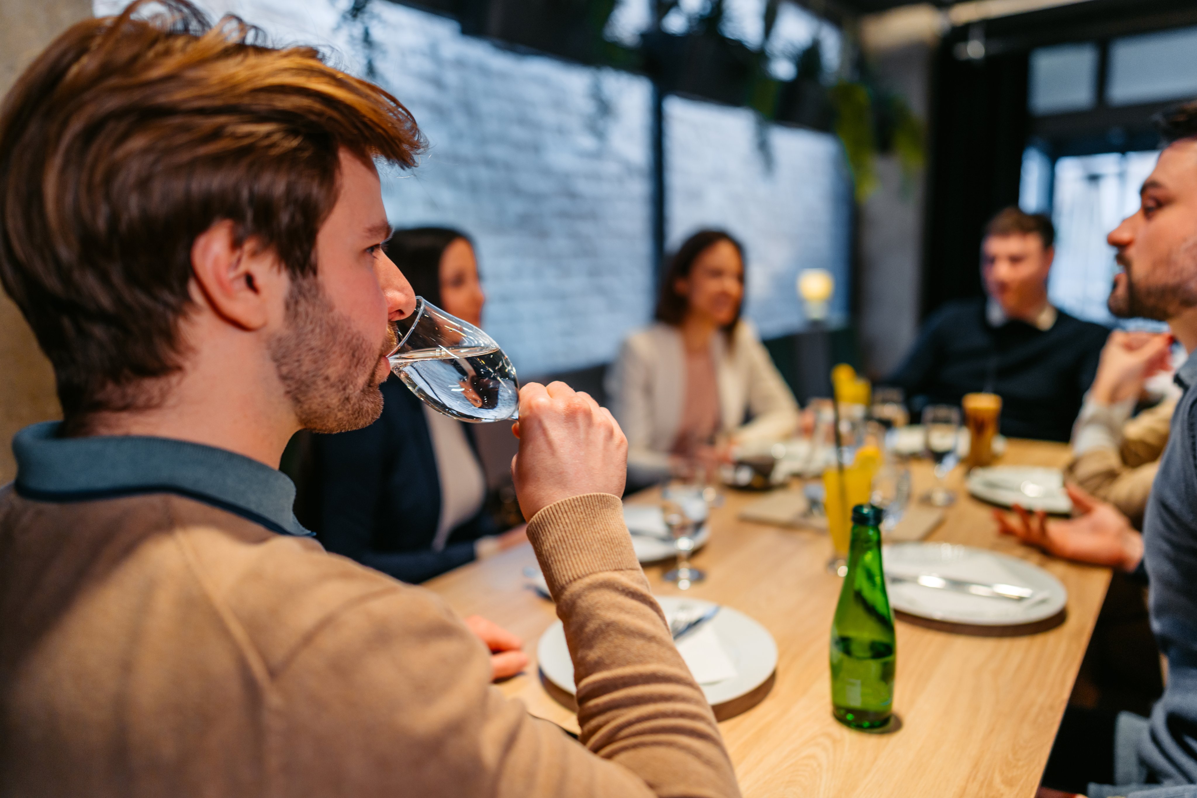 A man drinks water while sharing a meal with others
