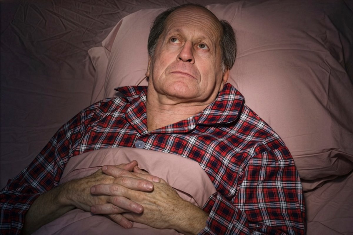 An older man laying in bed and looking up at the ceiling