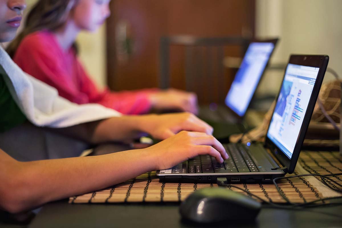 Children sitting in a row with computers in front of them during a class