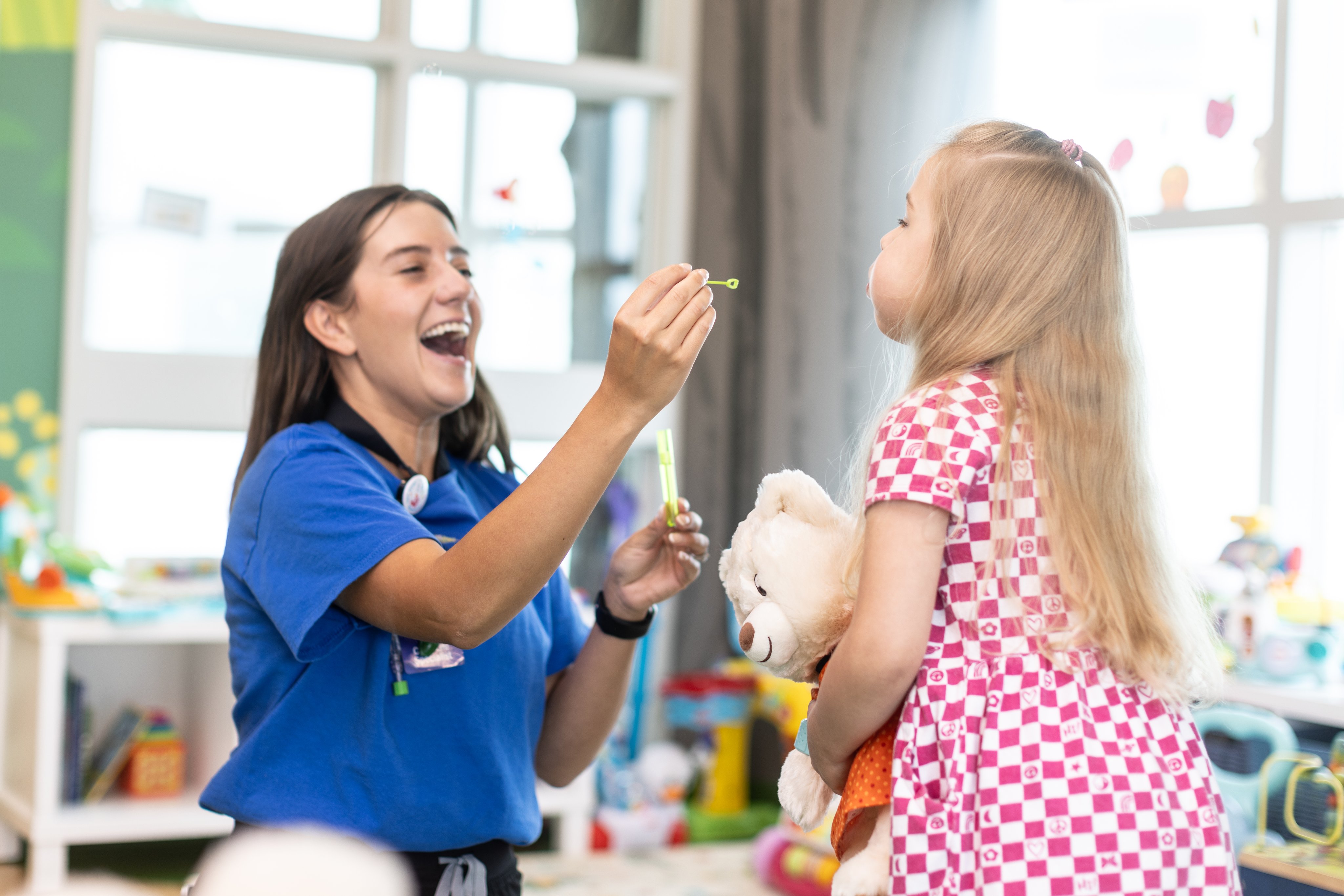 Child Life specialist holds bubble wand while little girl blows bubbles in hospital